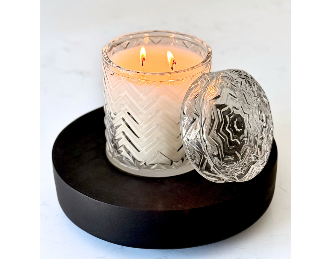 Candle in a textured glass holder on a black coaster with a white background