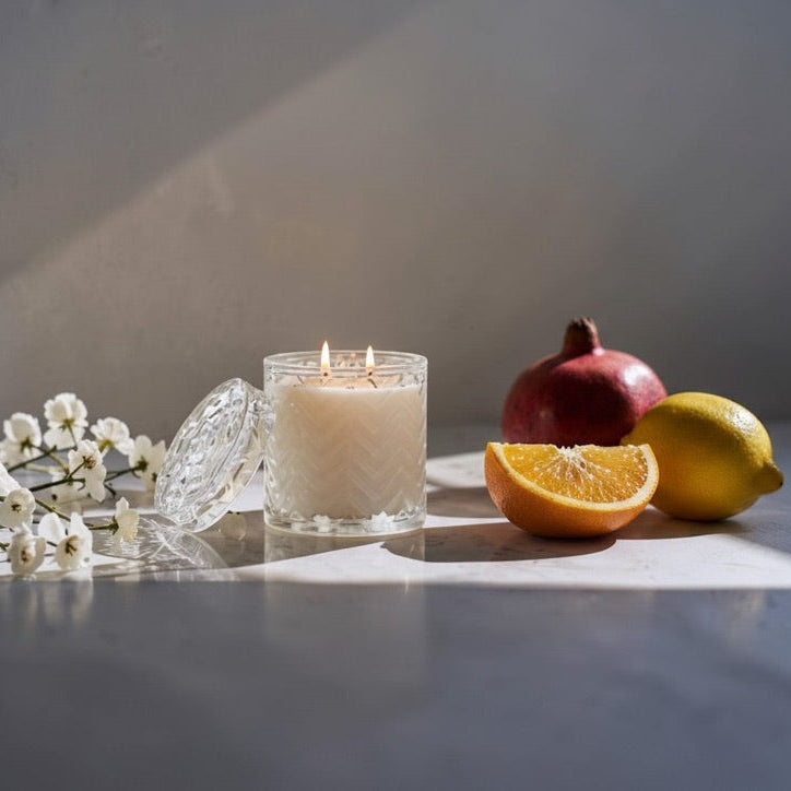 Clear glass candle with chevron embossed pattern next to cut orange, lemon and pomegranate.