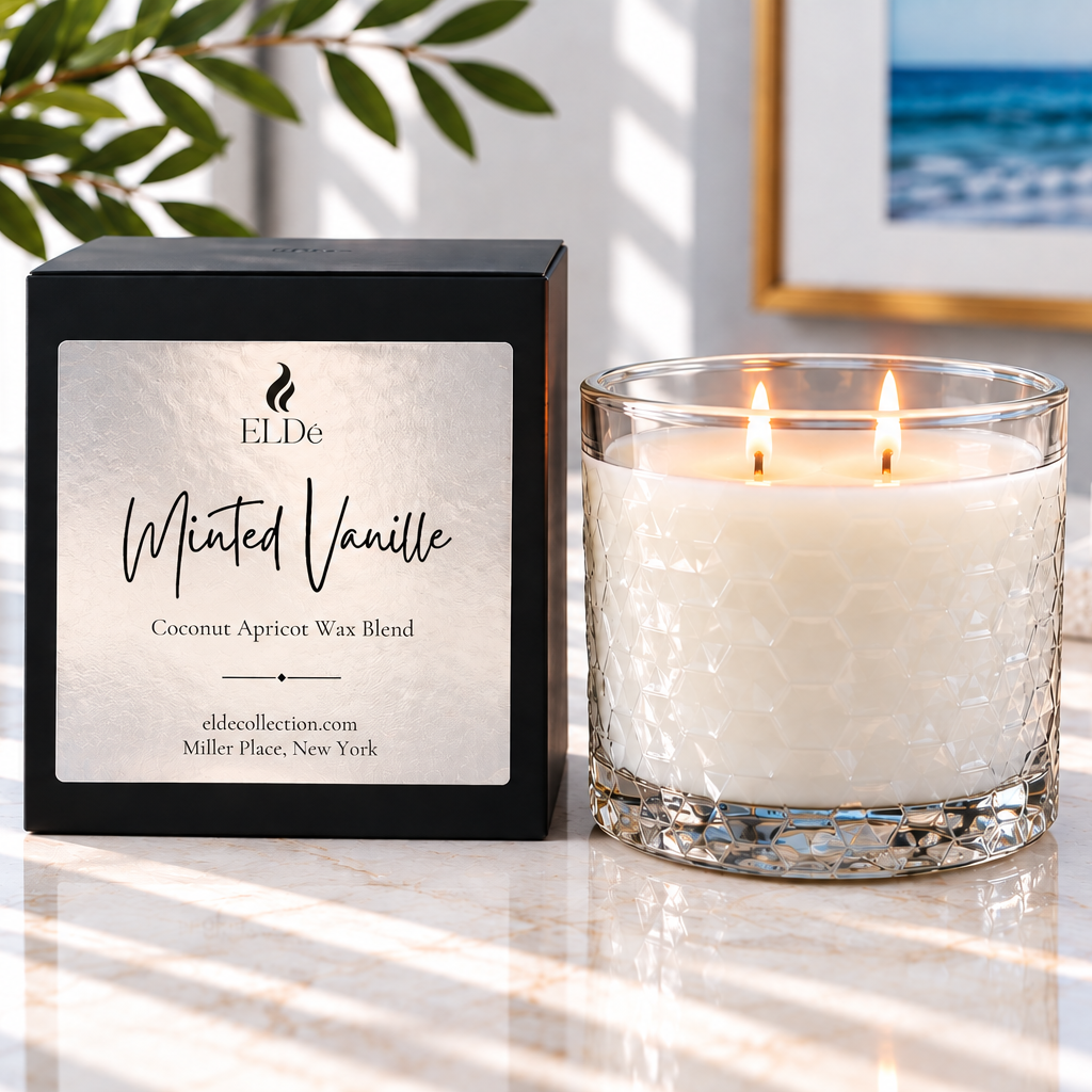 ELDe Collection 'Minted Vanille' scented candle in a clear textured glass jar with two lit wicks, shown next to its black packaging box on a marble surface with soft window light.