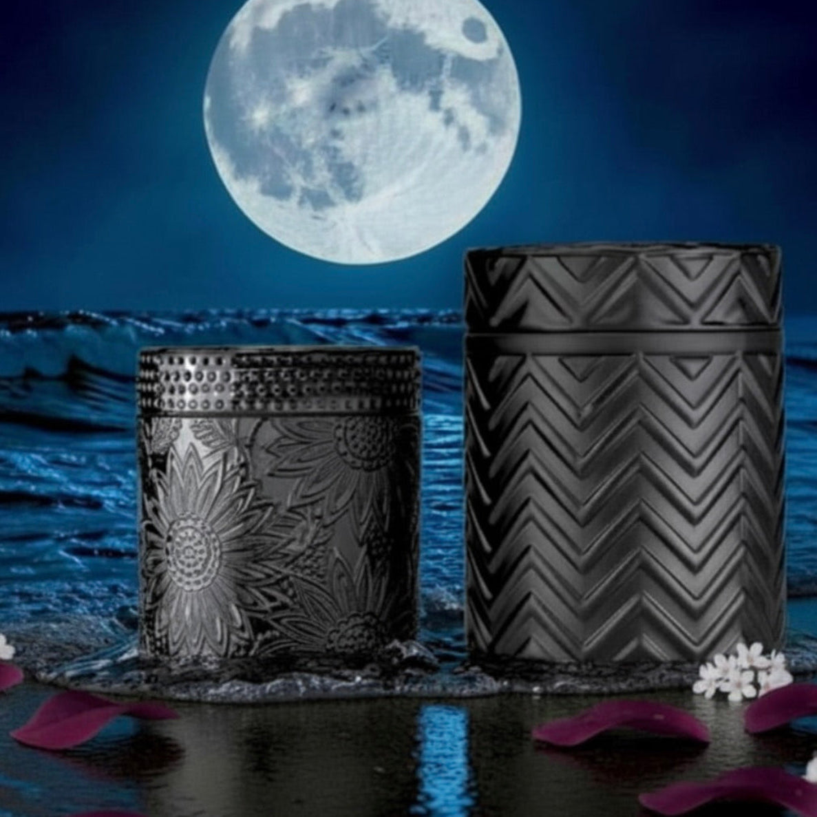 Two black decorative metal tins with embossed floral and chevron patterns, set in shallow water under a full moon with blue waves and scattered purple petals.