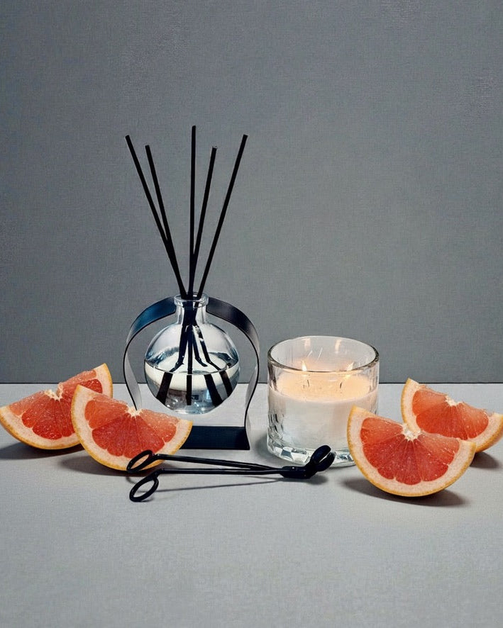 Diffuser with black sticks, sliced grapefruit, and a candle on a gray surface.