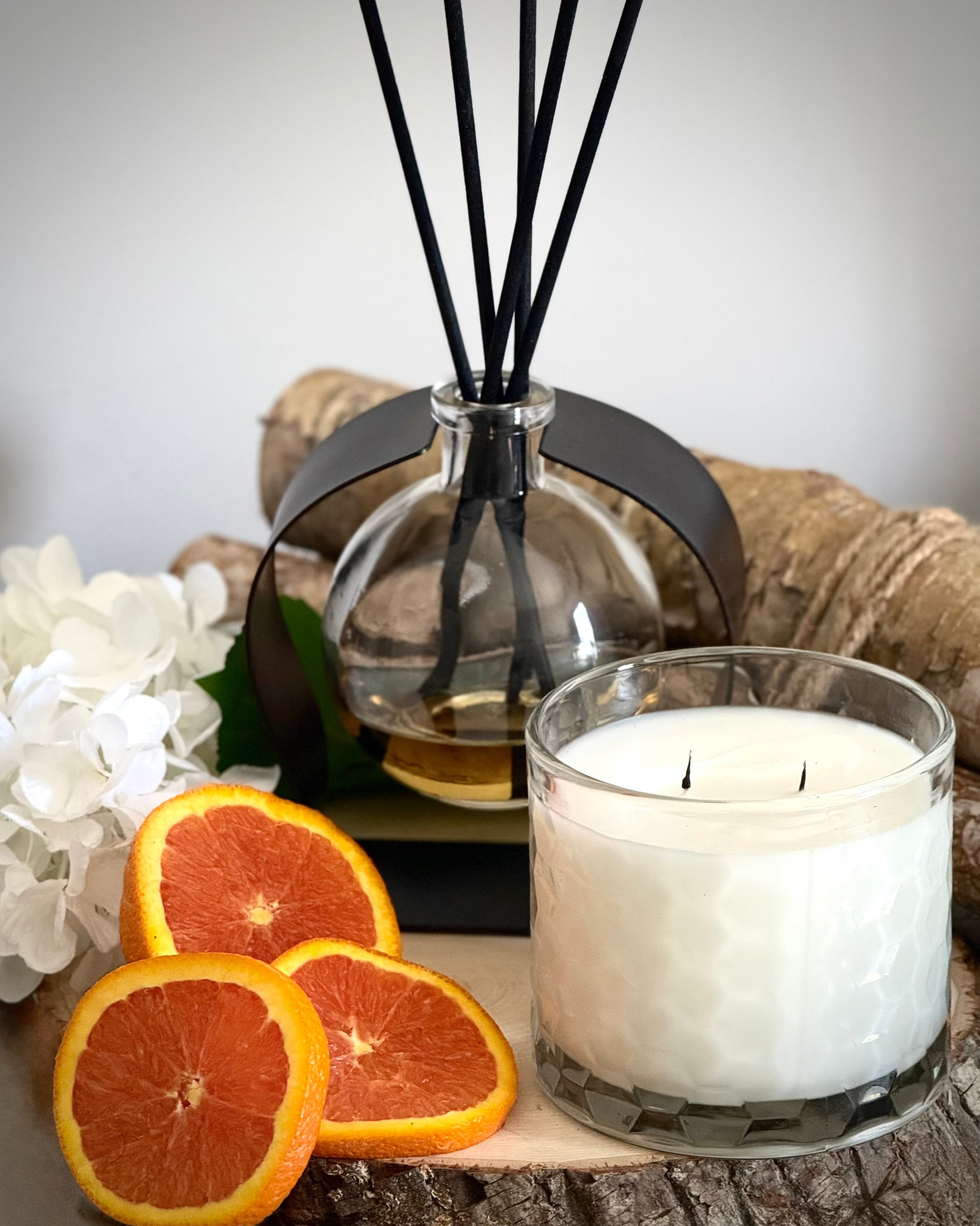 Aromatherapy diffuser with reeds, a candle, and sliced oranges on a wooden surface.