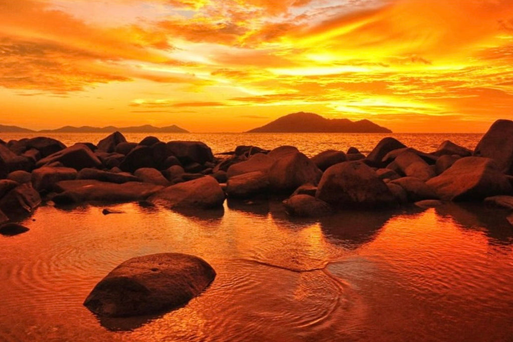 Sunset over a rocky beach with warm orange hues representing Amber Coast  scent