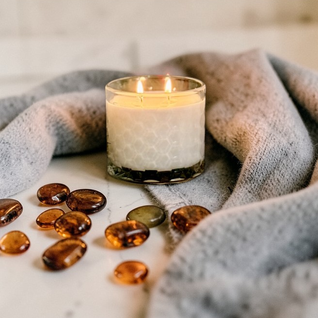 Candle in a glass holder with amber-colored stones on a textured surface