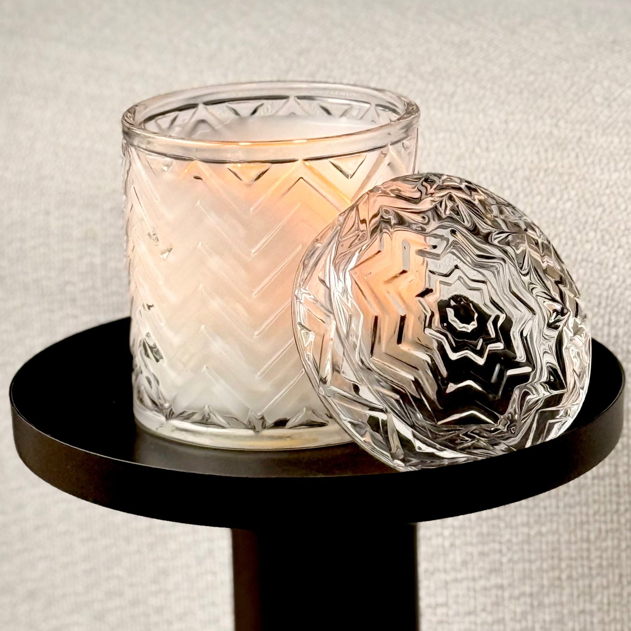 Decorative glass candle holder with a lit candle on a small round black table.