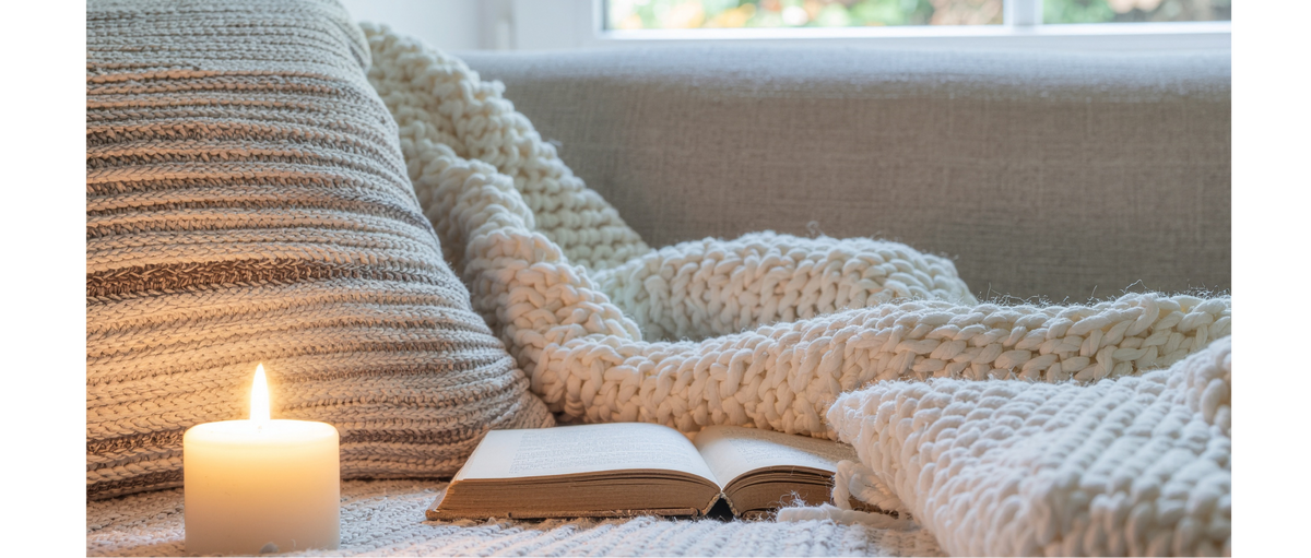 Cozy reading nook with a blanket, book, and candle on a couch.