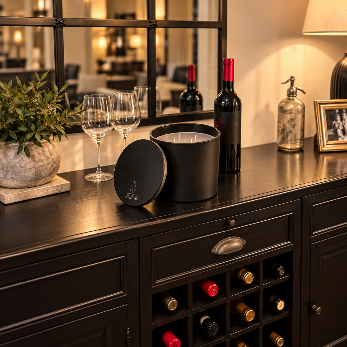ELDé Fireplace Candle displayed with its matching lid on a black wine buffet, with a wine bottle and glasses showing its substantial size.