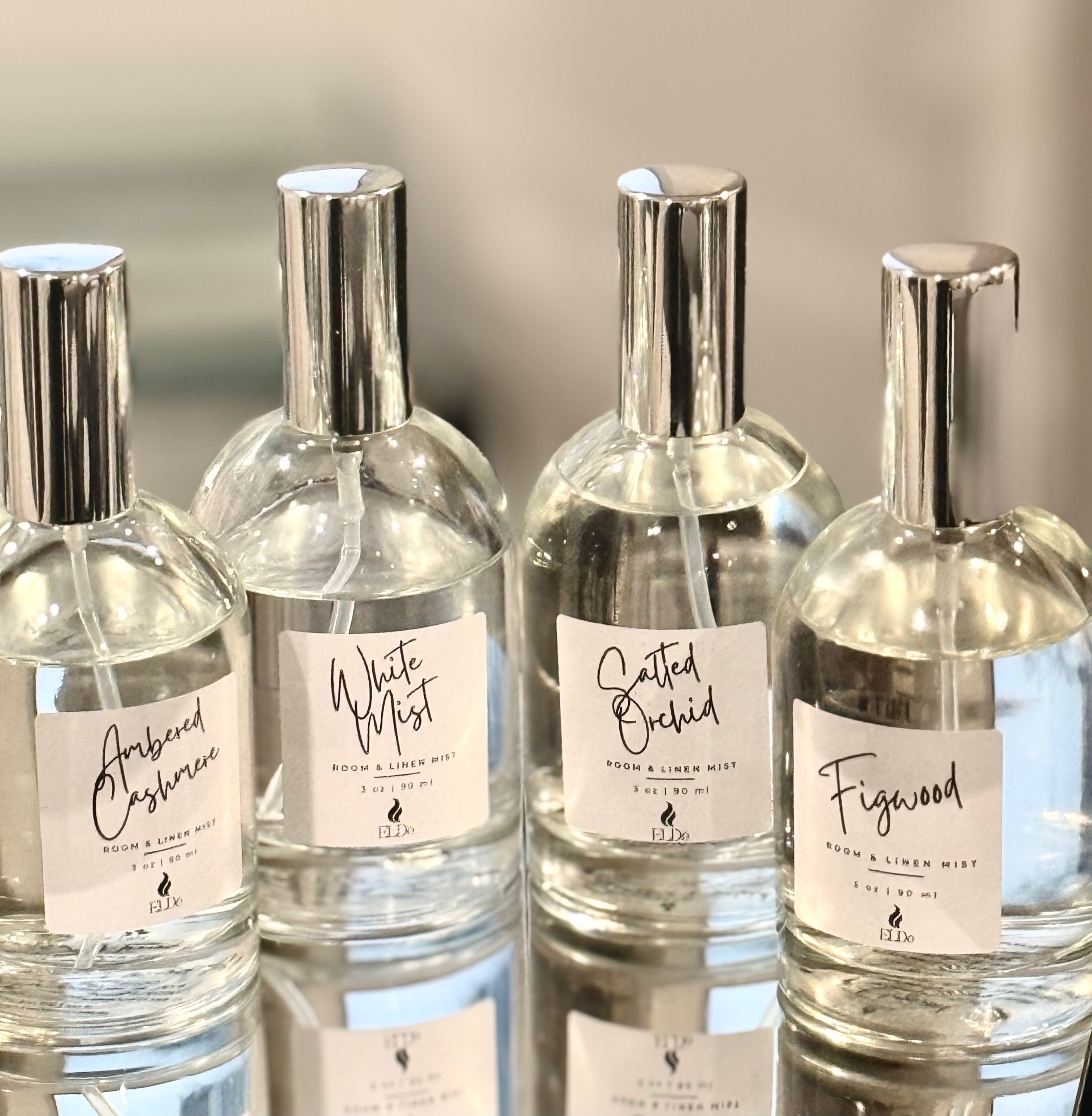 Four clear perfume bottles with silver caps and labels on a reflective surface.