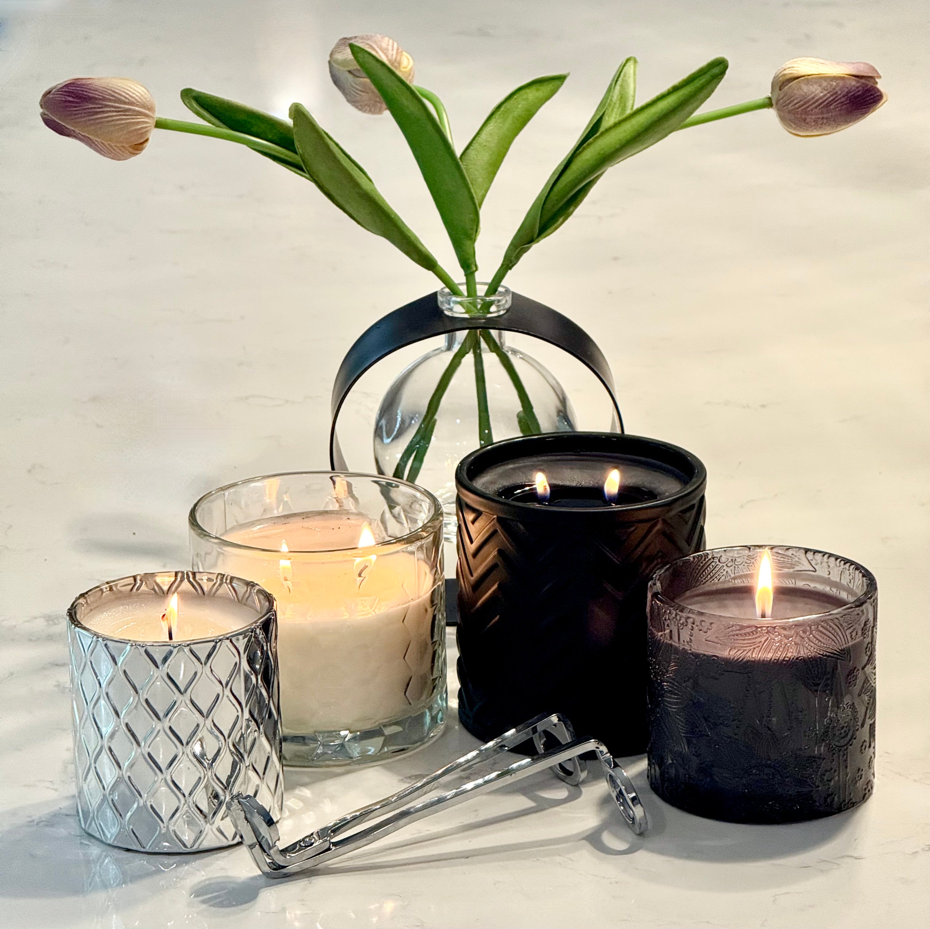 Four candles in different holders with a diffusers of tulips on a light background