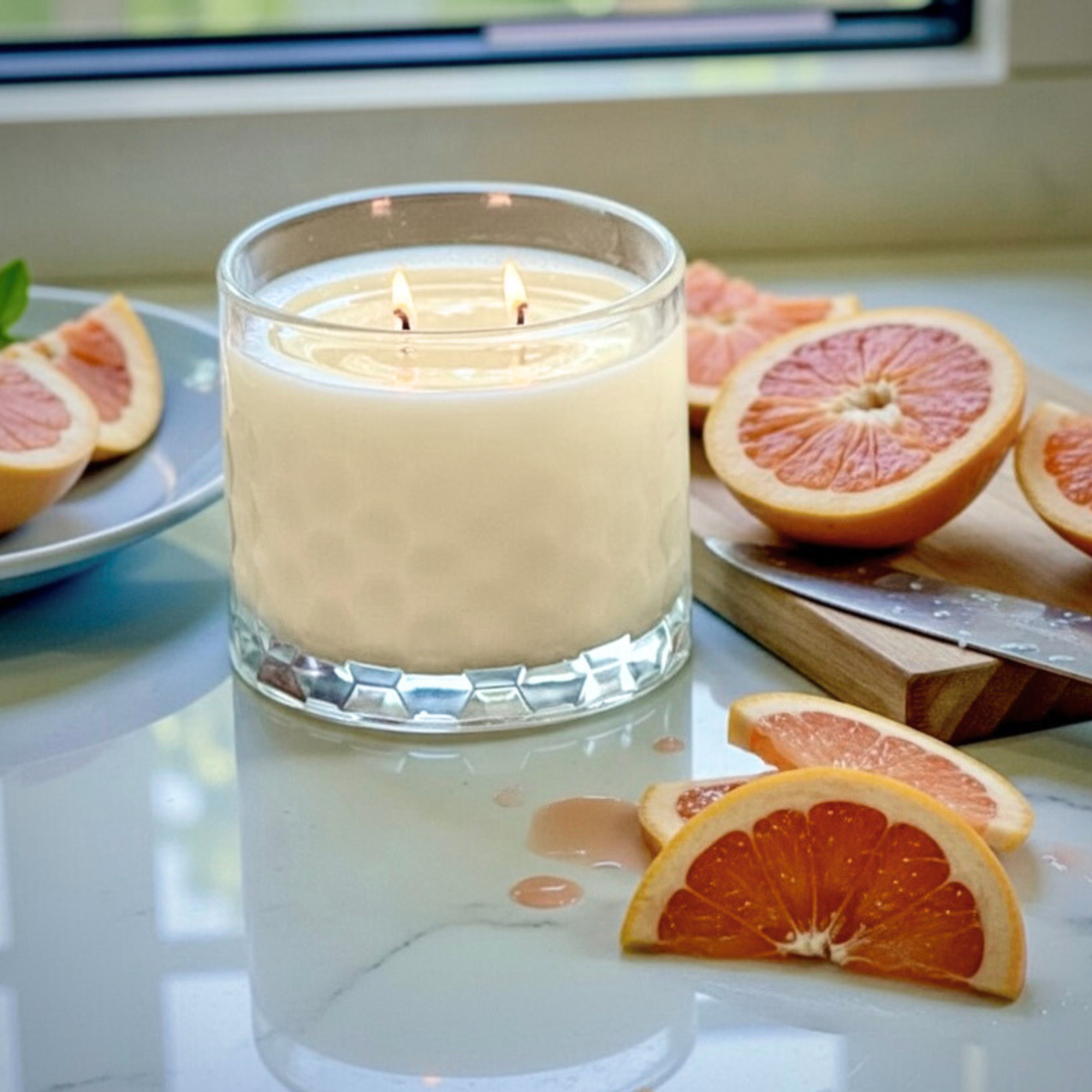 grapefruit scented candle on countertop with cut slices of grapefruit