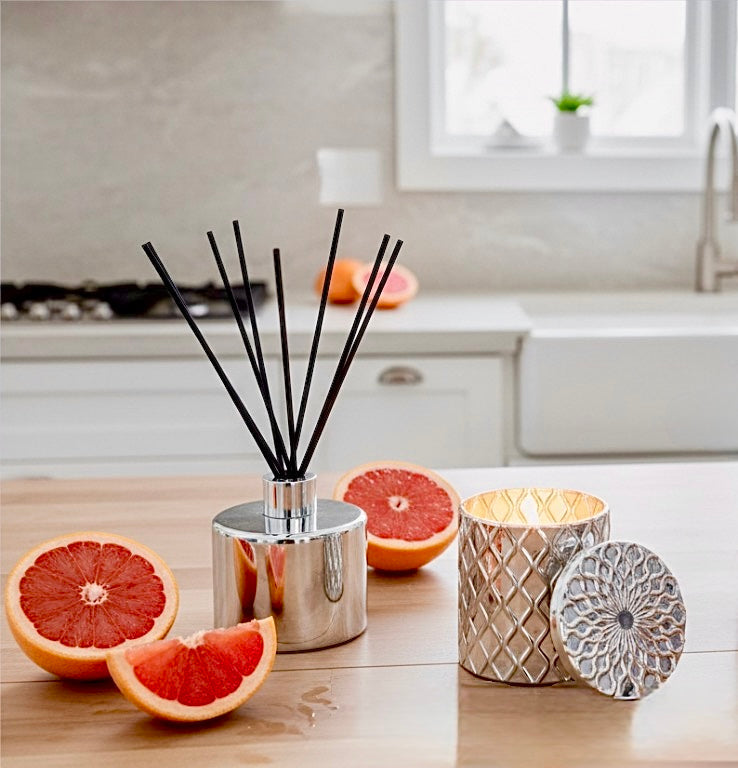 Diffuser with black sticks and decorative candle on a kitchen counter with grapefruits.