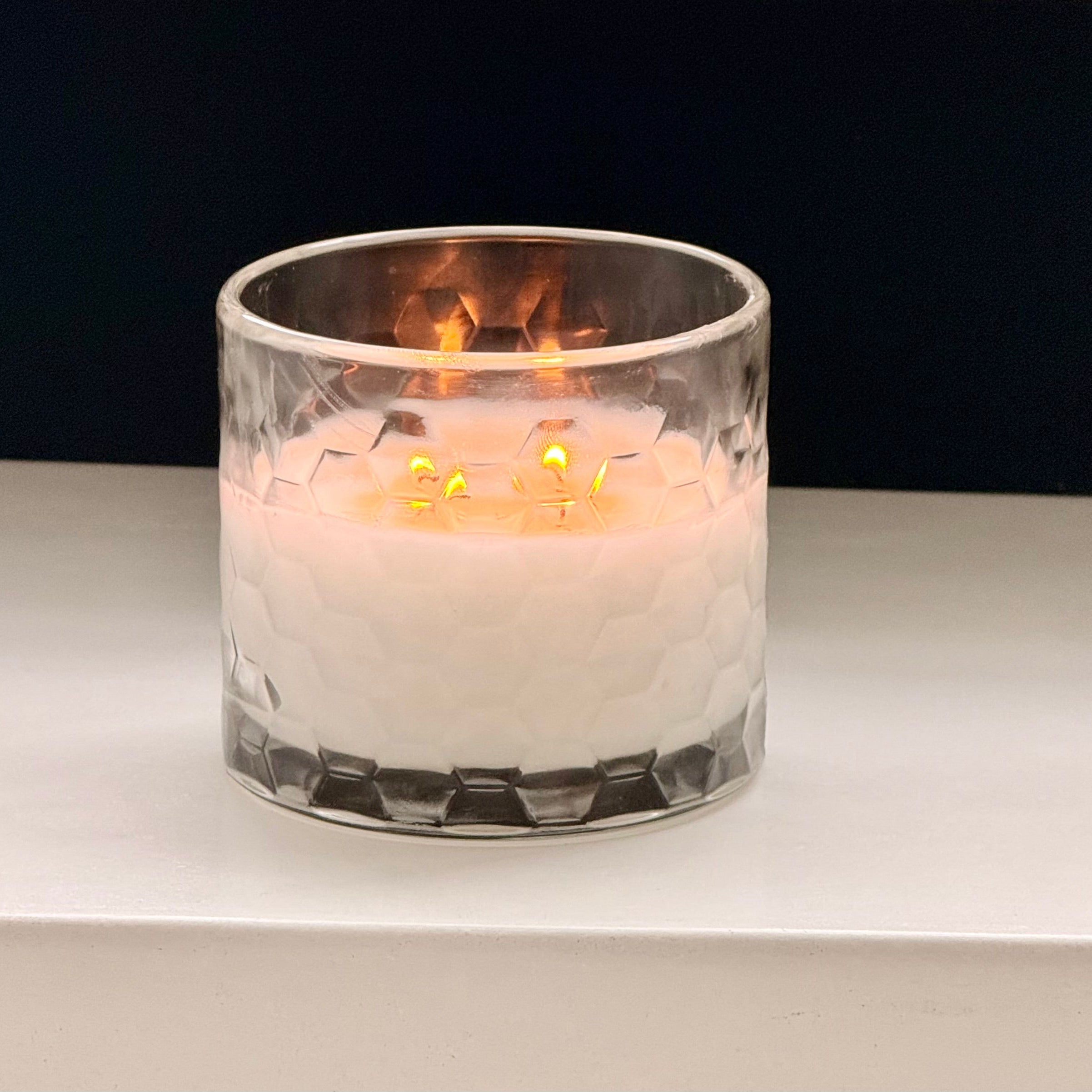 Candle in a glass holder on a white surface with a dark background