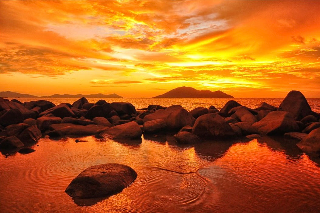 Rocks on a shore with an orange-colored sky representing Hexaglow Amber Coast candle scent