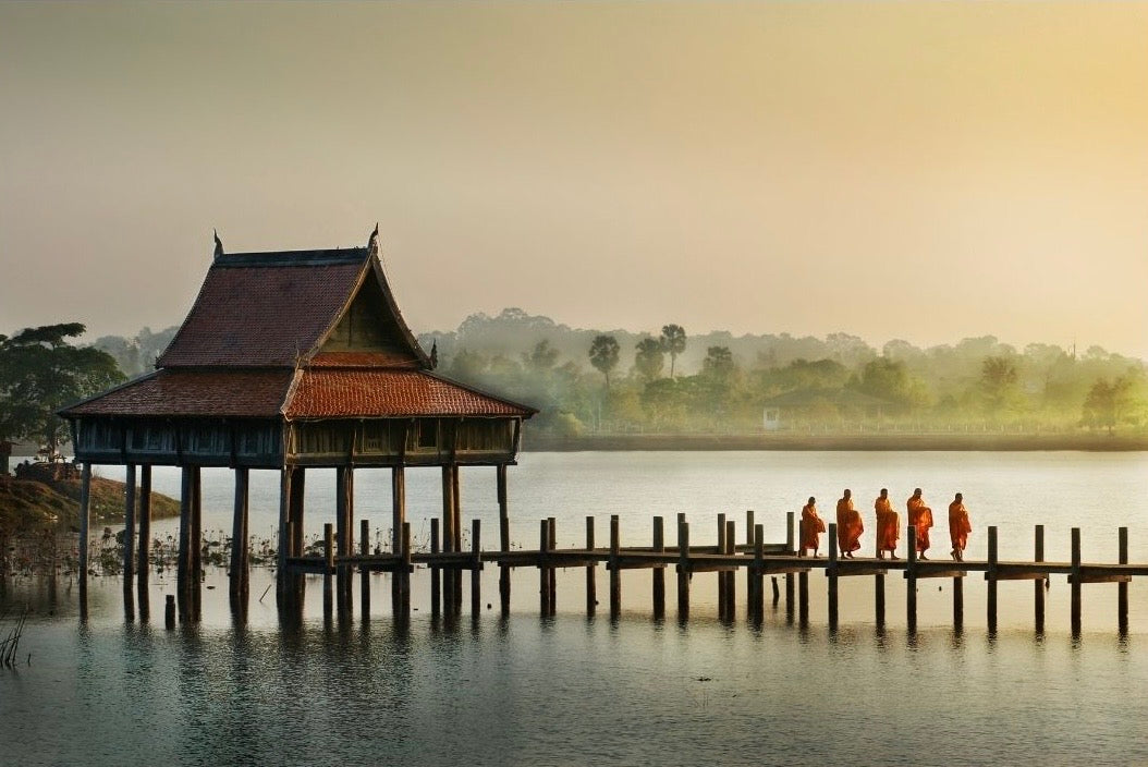 Mahogany hut on stilts over water with people walking along the pier representing Hexaglow Woodland & Mahogany Teak candle scent