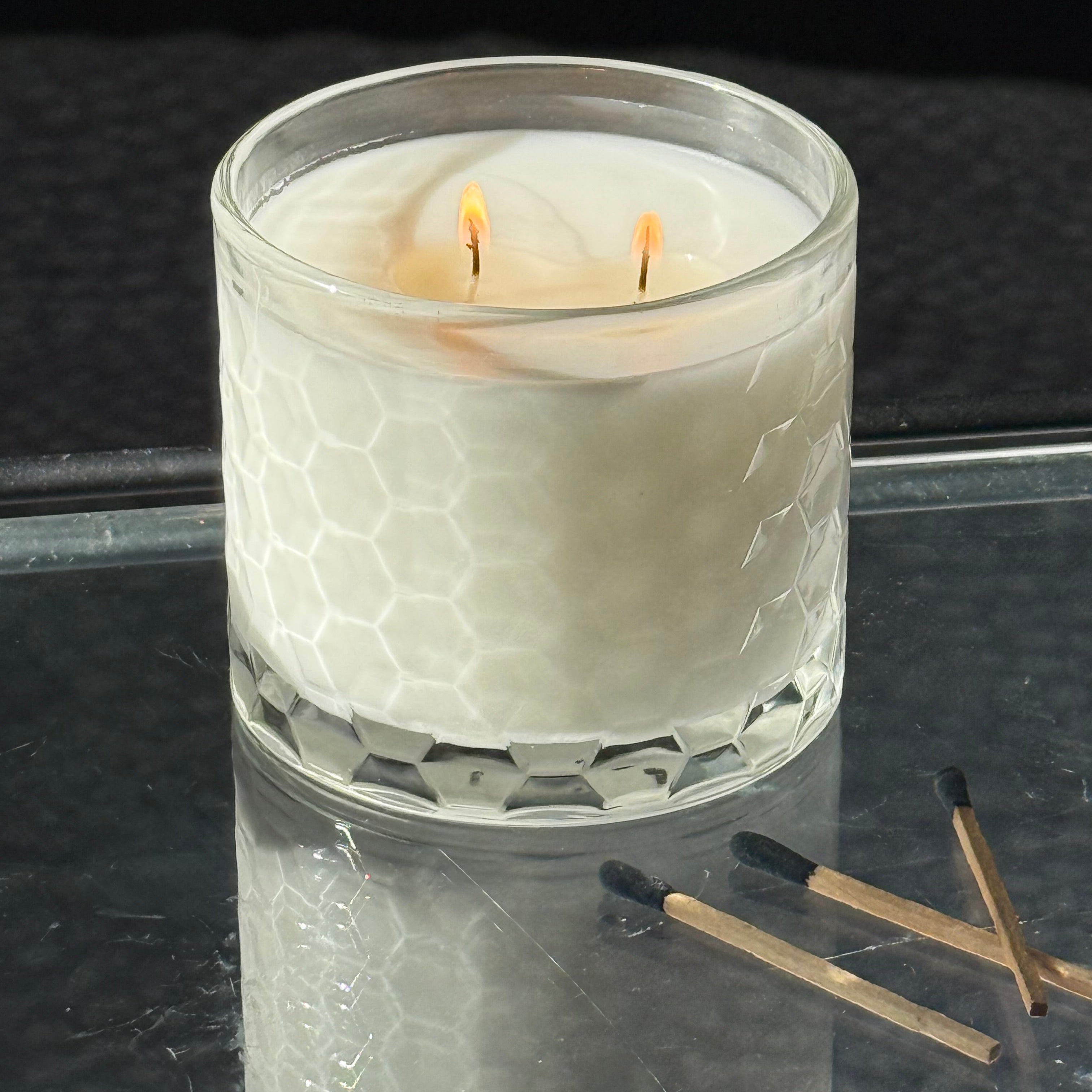 Candle in a textured glass holder with matches on a reflective surface
