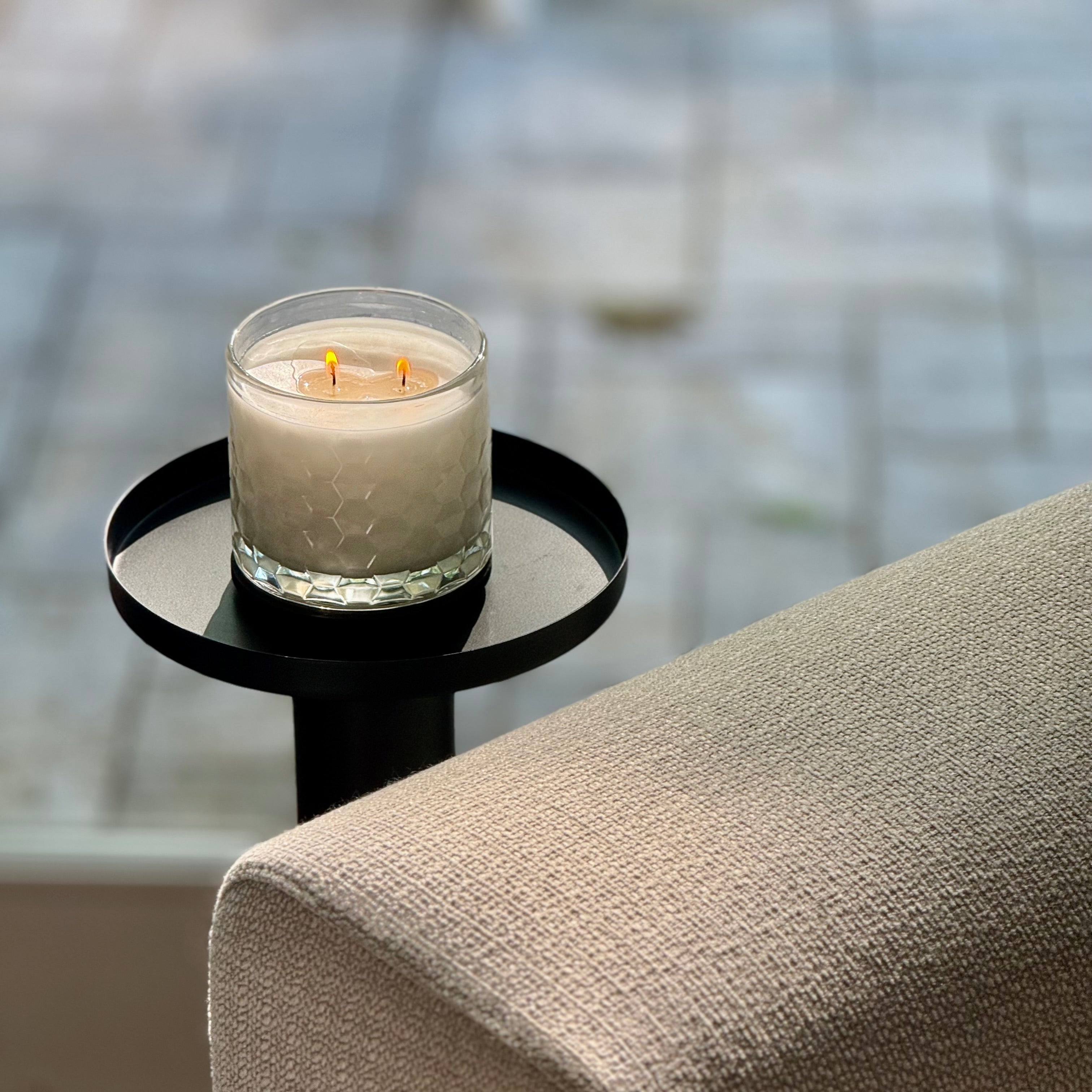 Candle in a glass holder on a small round table next to a beige sofa with a blurred background