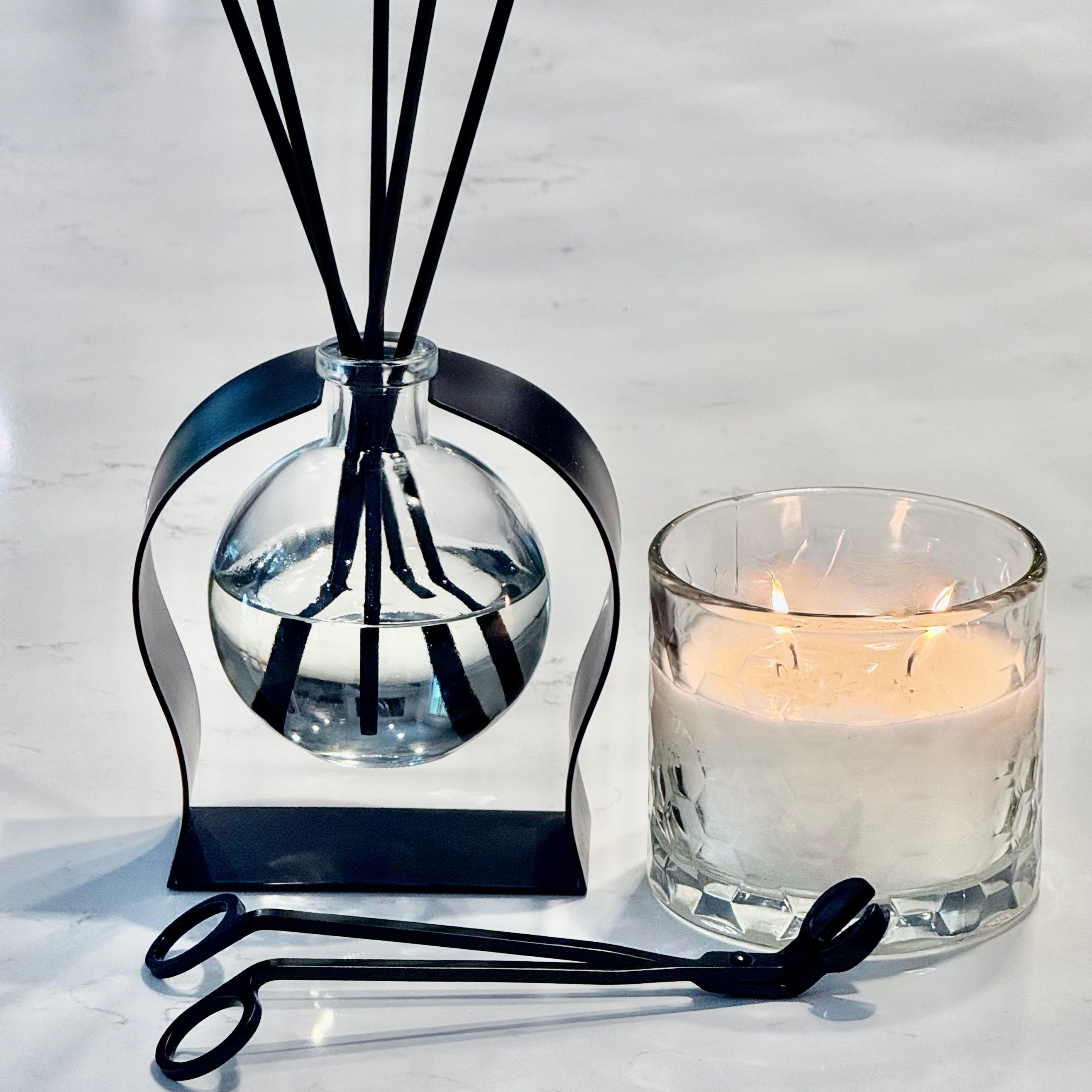 A diffuser with black sticks and a candle on a white surface