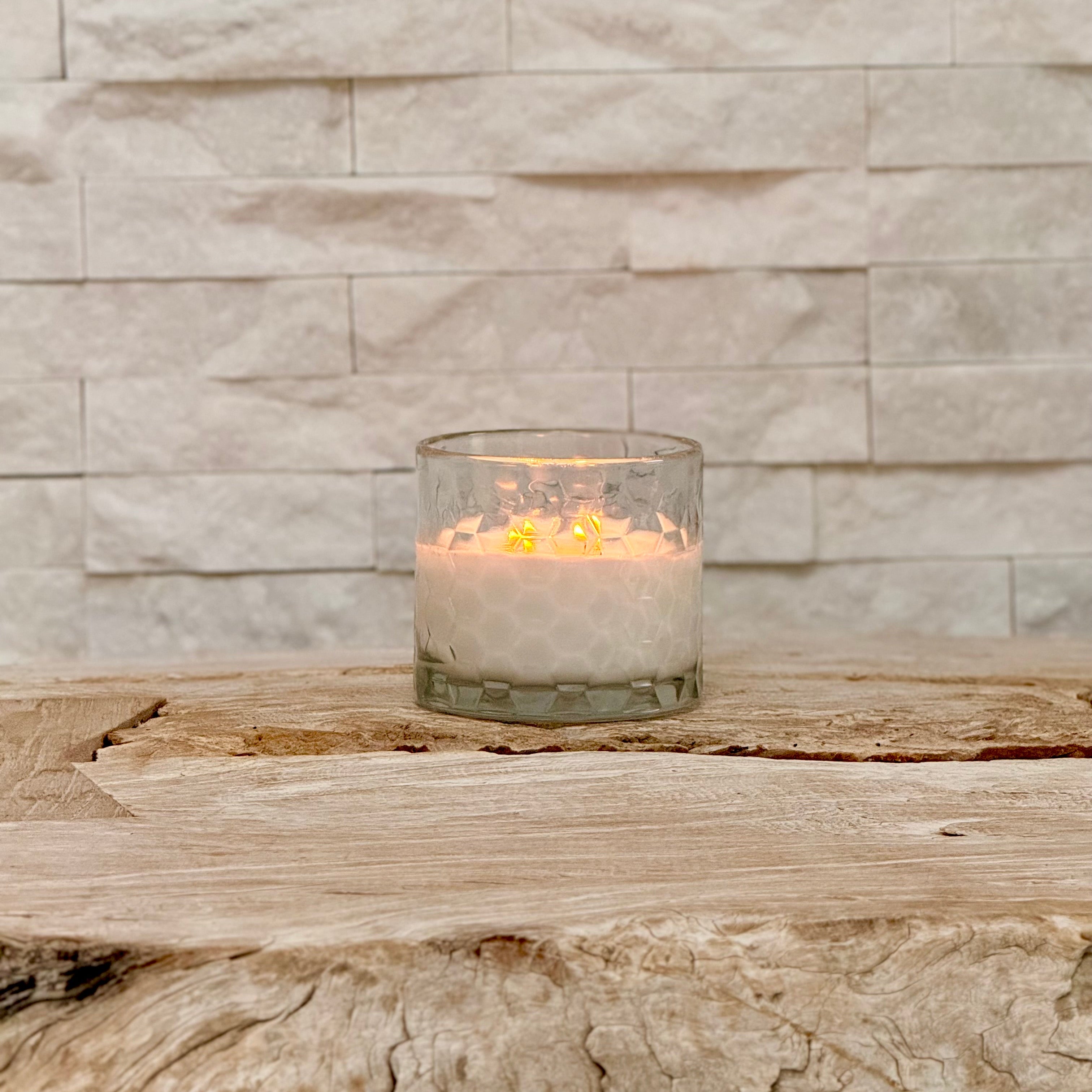 Candle in a glass holder on a wooden surface with a stone wall background
