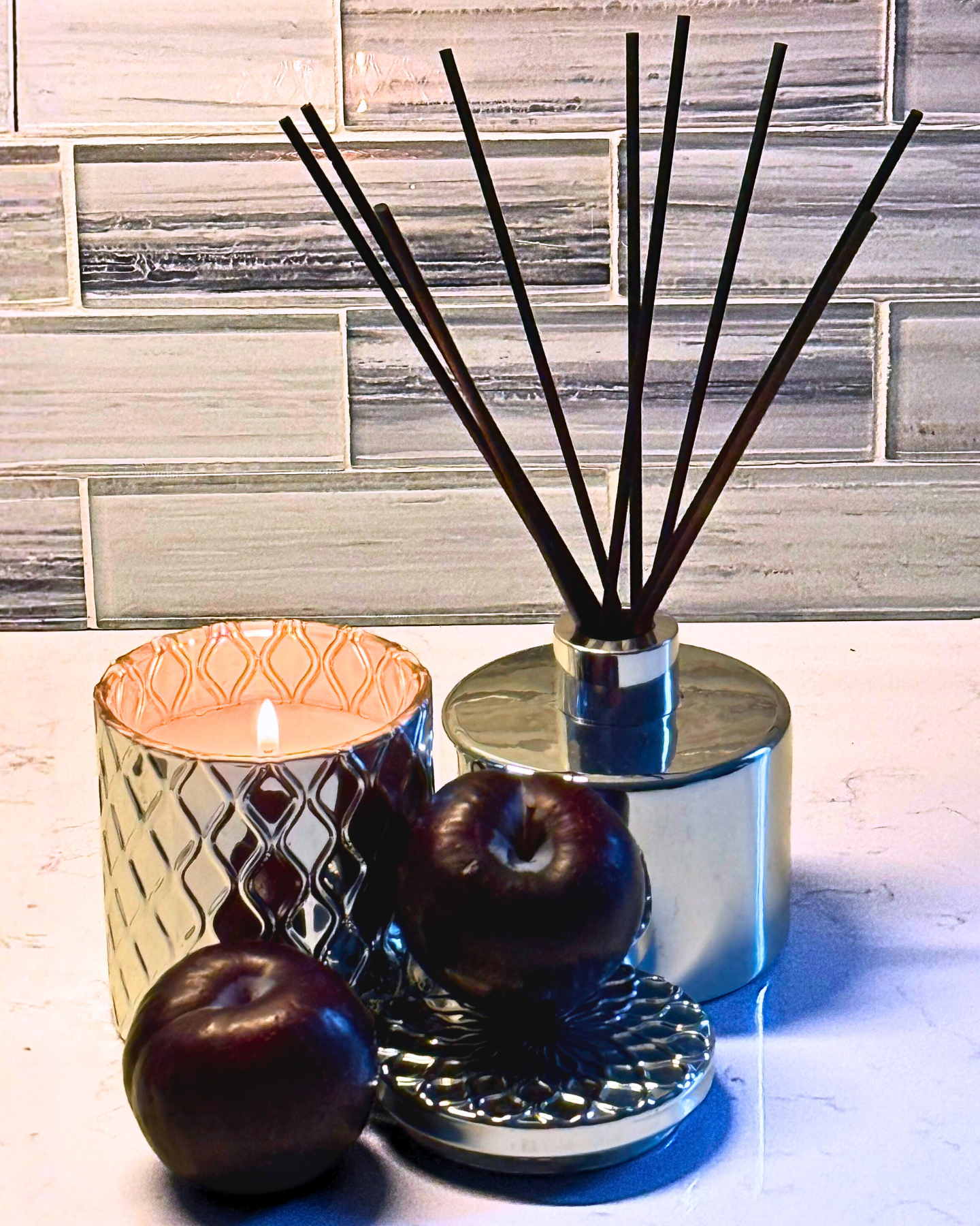 Diffuser with reeds and a candle on a marble surface with a tiled wall background