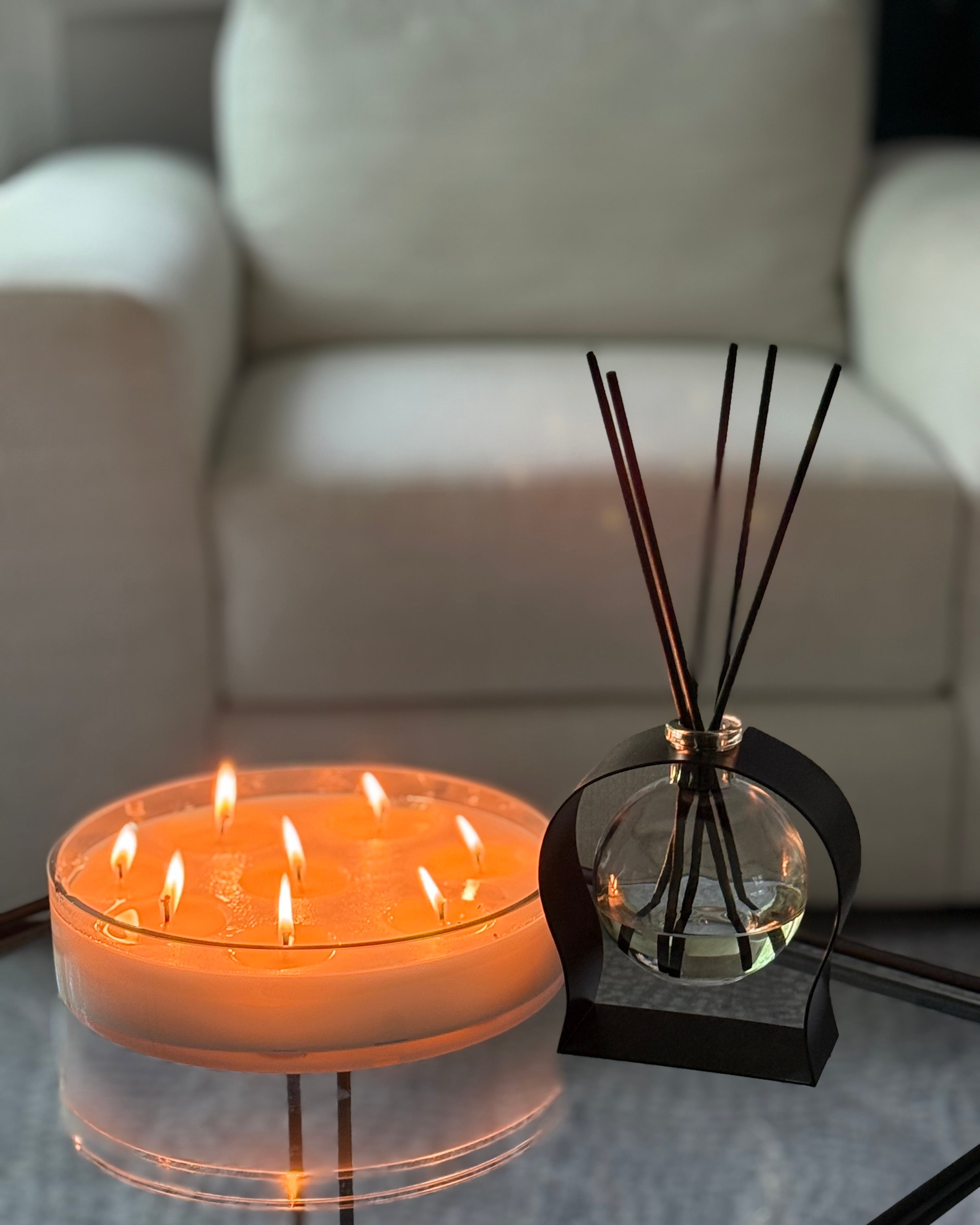 Candle with three flames and a diffuser on a table in a living room setting.