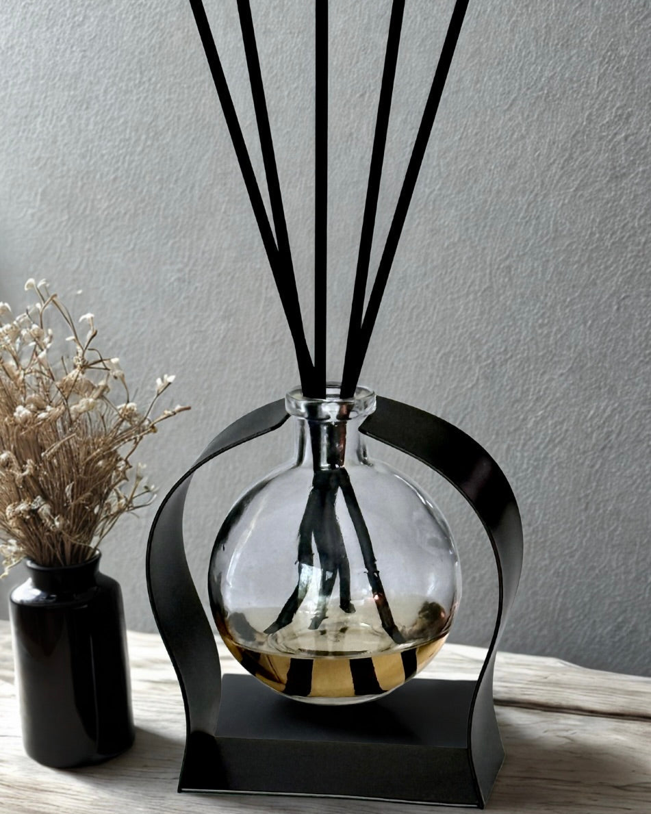 A glass diffuser with black sticks on a decorative stand against a gray wall.