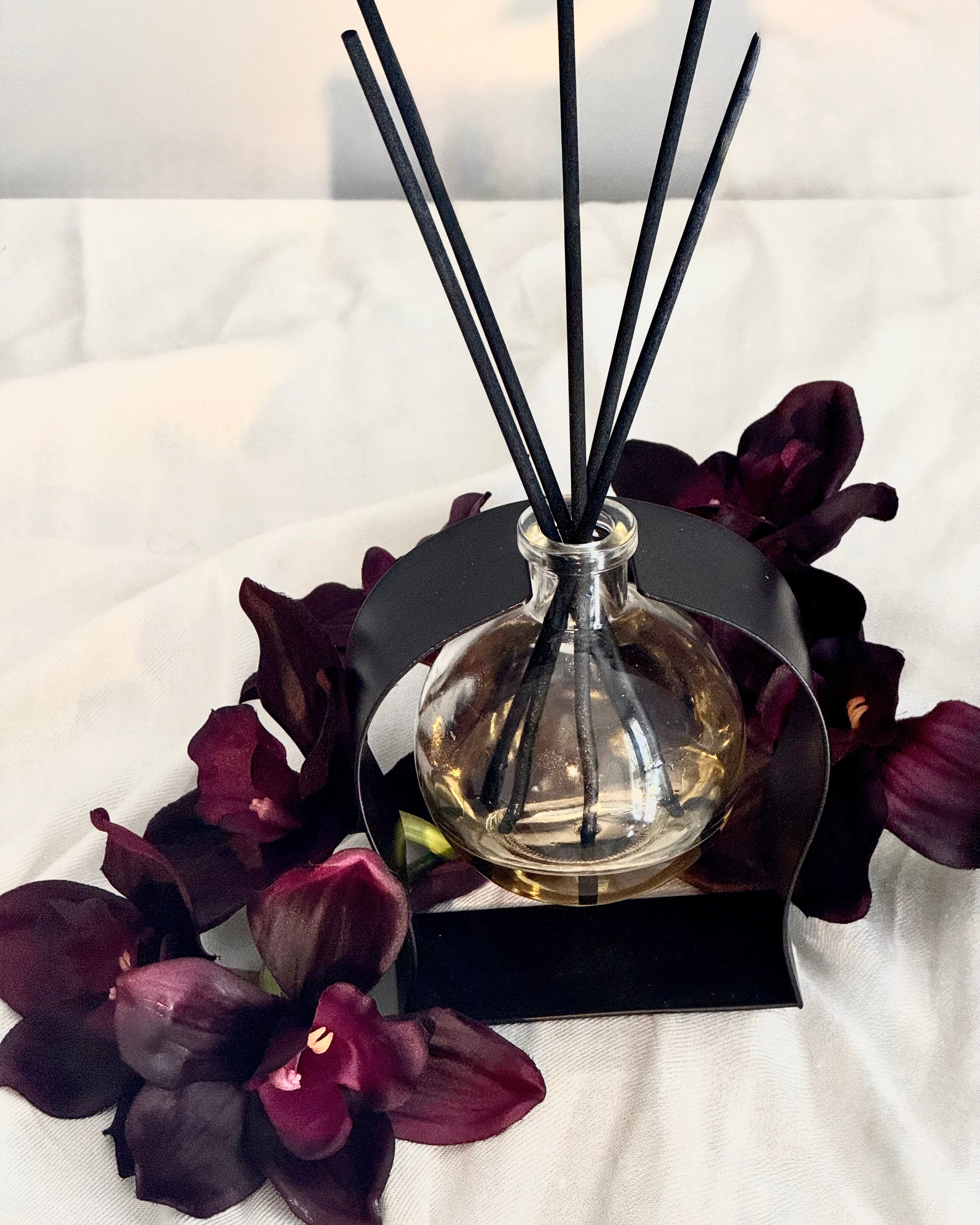 Aromatherapy diffuser with black sticks and dark purple flowers on a white surface