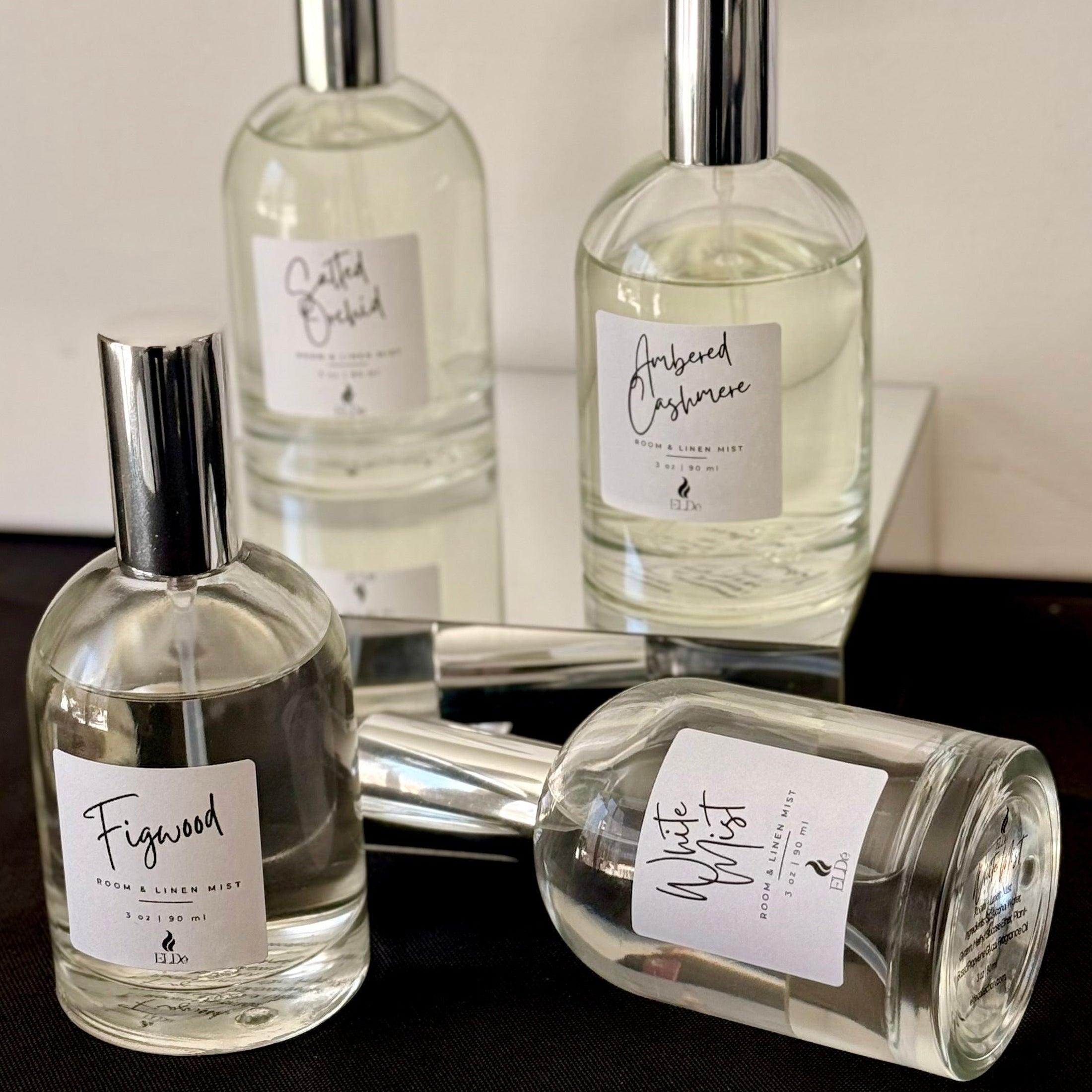 Four perfume bottles with labels on a reflective surface.