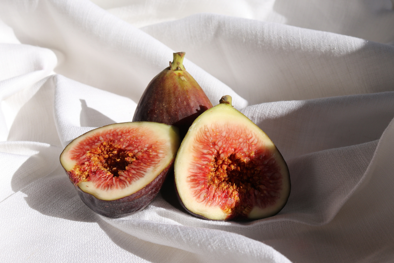 Two figs, one whole and one halved, on a white fabric background