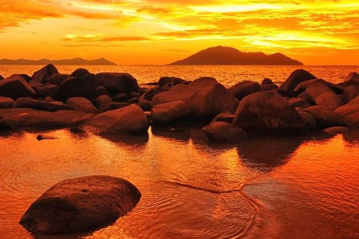 Sunset over a rocky beach with vibrant orange and yellow colors.