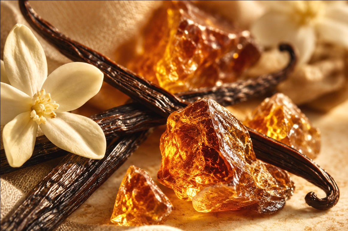 Vanilla beans and amber-colored vanilla crystals arranged on a beige fabric surface with a white vanilla blossom in the foreground.