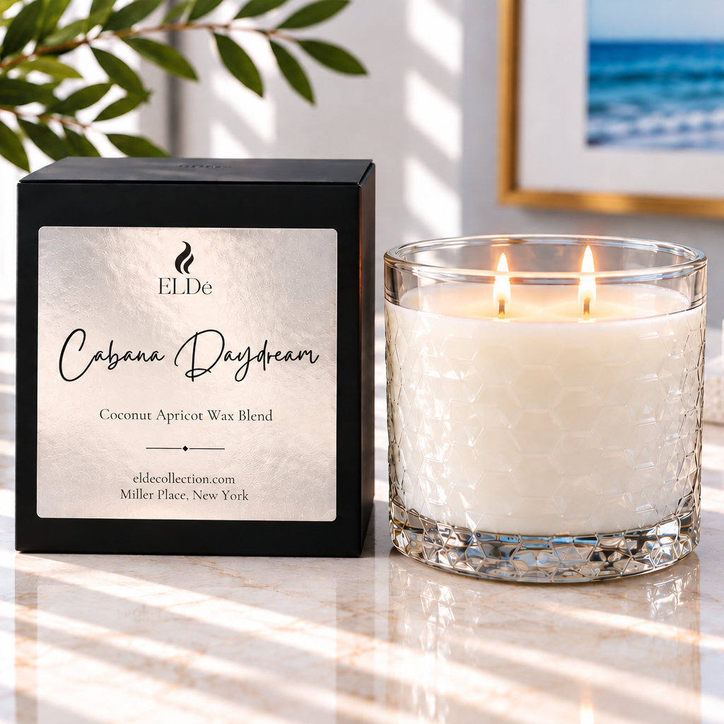 A lit double-wick candle in a textured glass jar sits beside its black branded box on a marble surface. The label reads ELDe and 'Cabana Daydream Coconut Apricot Wax Blend.