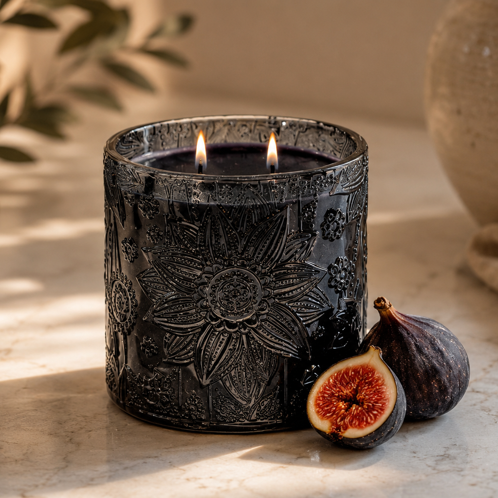 A dark charcoal gray embossed candle jar with two lit wicks, styled on a marble surface with figs and a ceramic vase in the background.