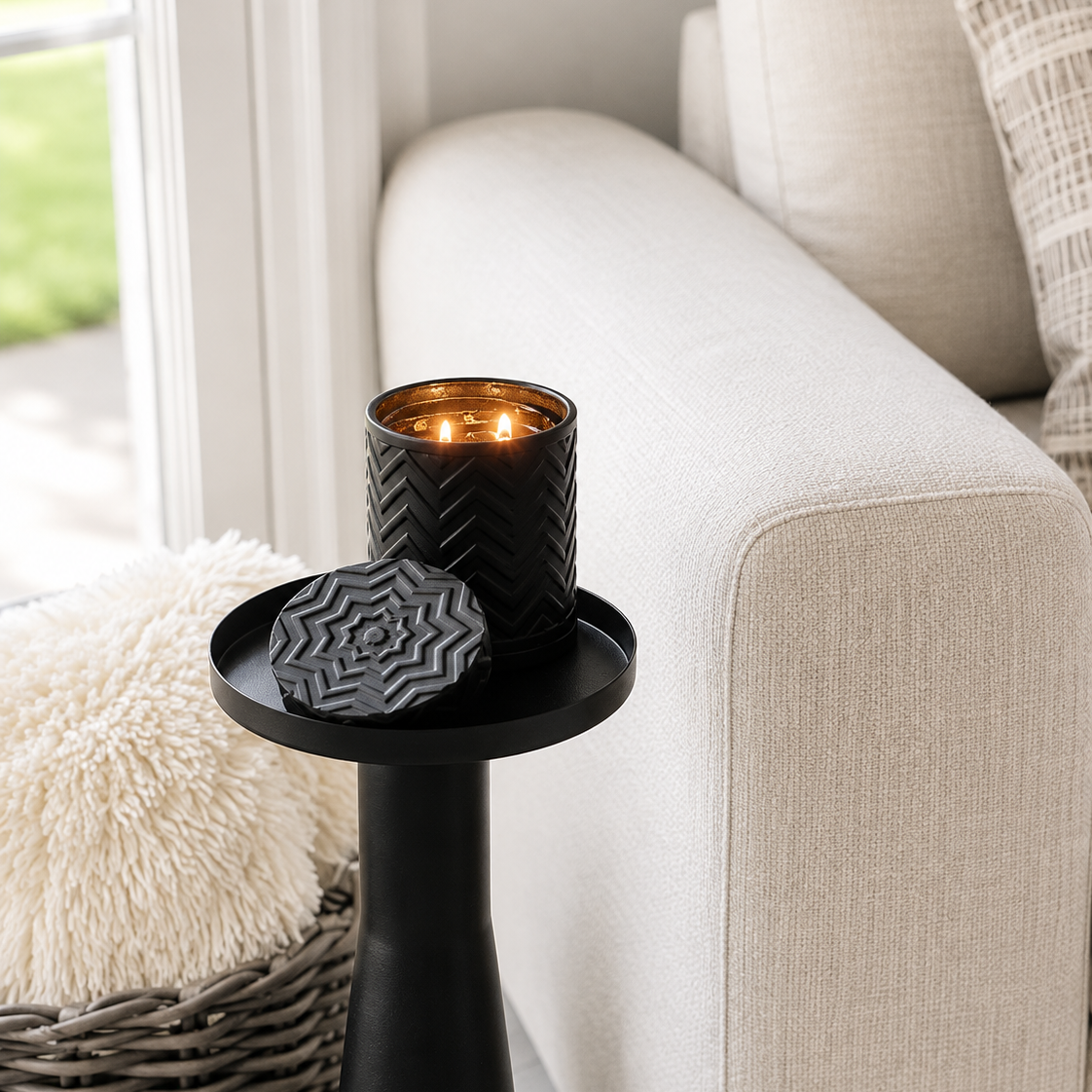 A black textured candle holder with a matching lid sits on a black side table next to a light beige sofa in a bright, modern living room.