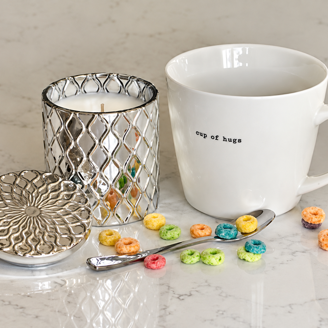 SilverScape candle next to white mug reading cup of hugs and scattered fruity cereal rings in front of both.