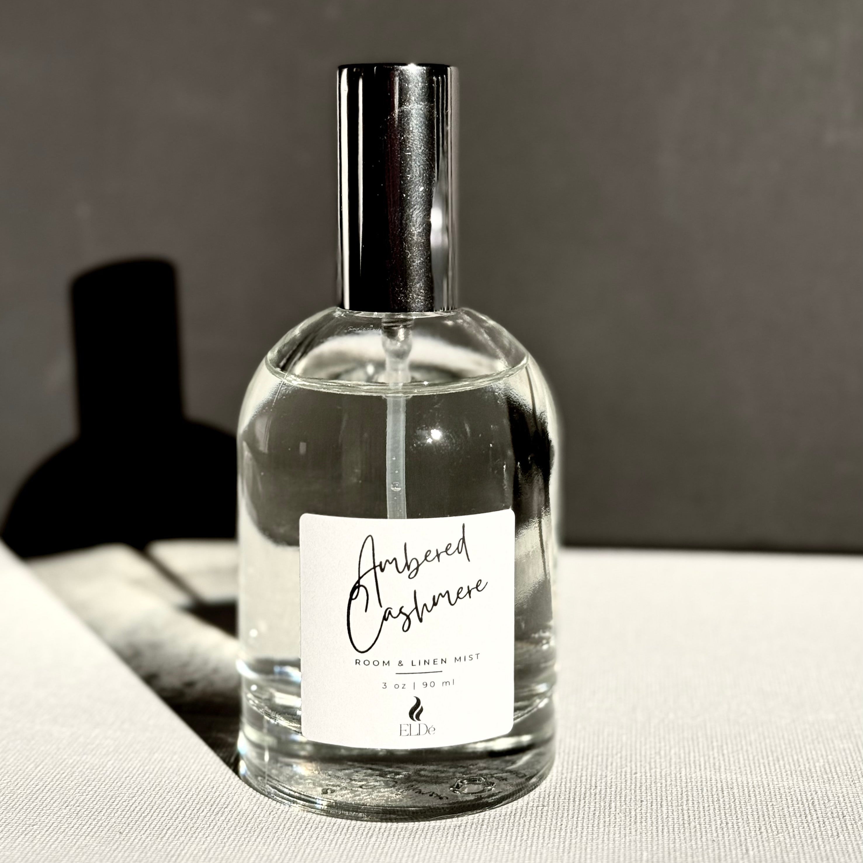 Perfume bottle labeled 'Ambered Cashmere' on a reflective surface with a dark background