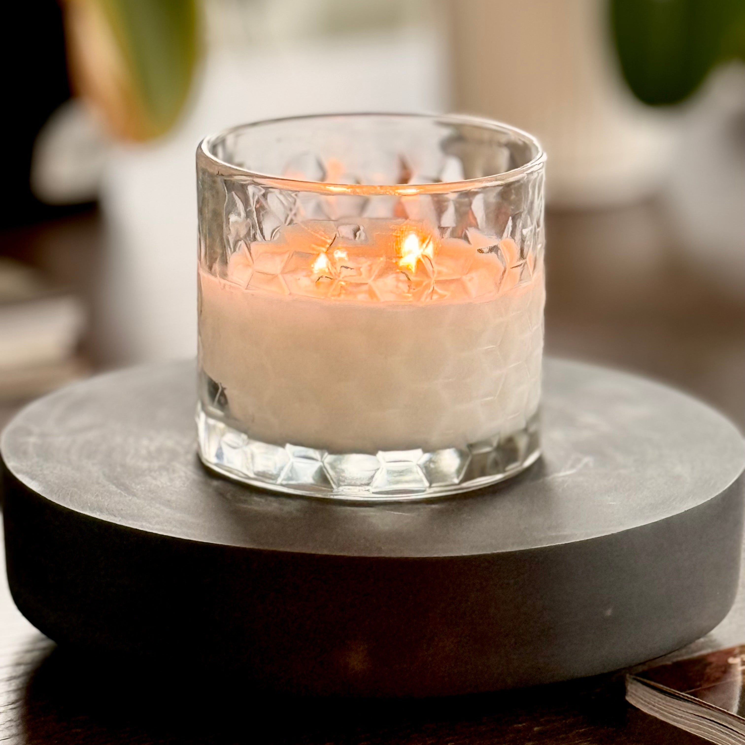 Candle in a glass holder on a dark stone coaster with a blurred background