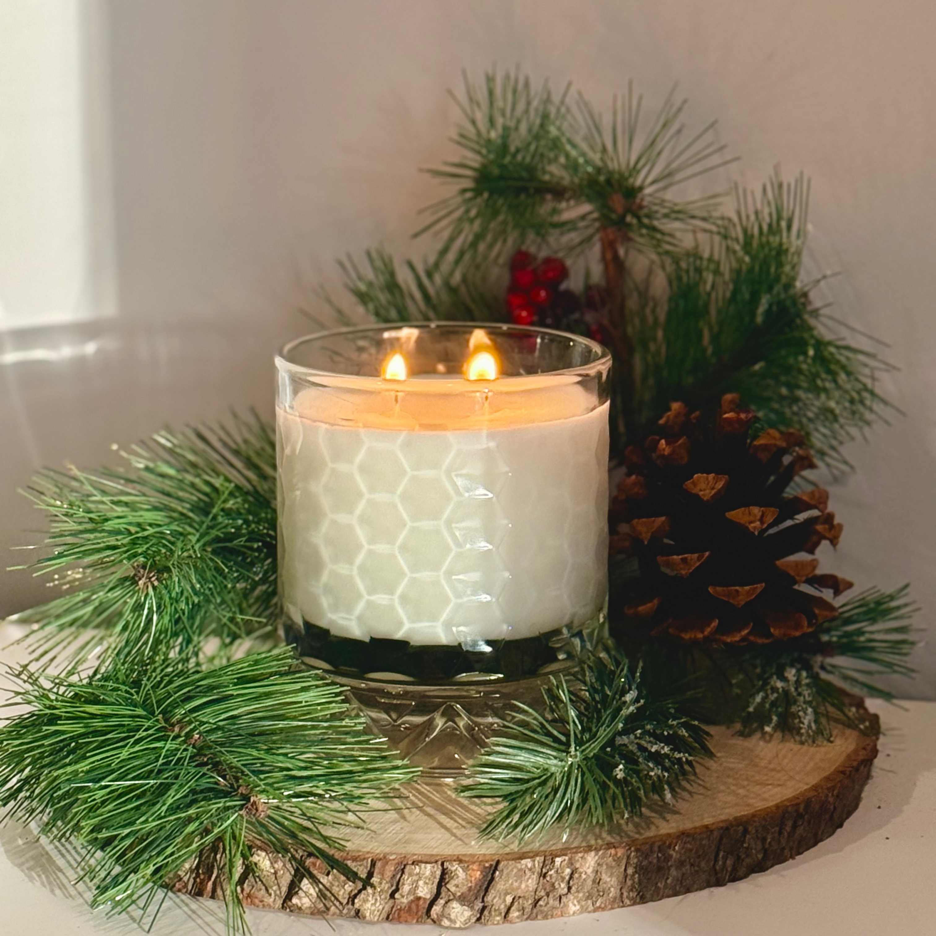 Candle in a glass holder on a wooden slice with pine branches and a pine cone.