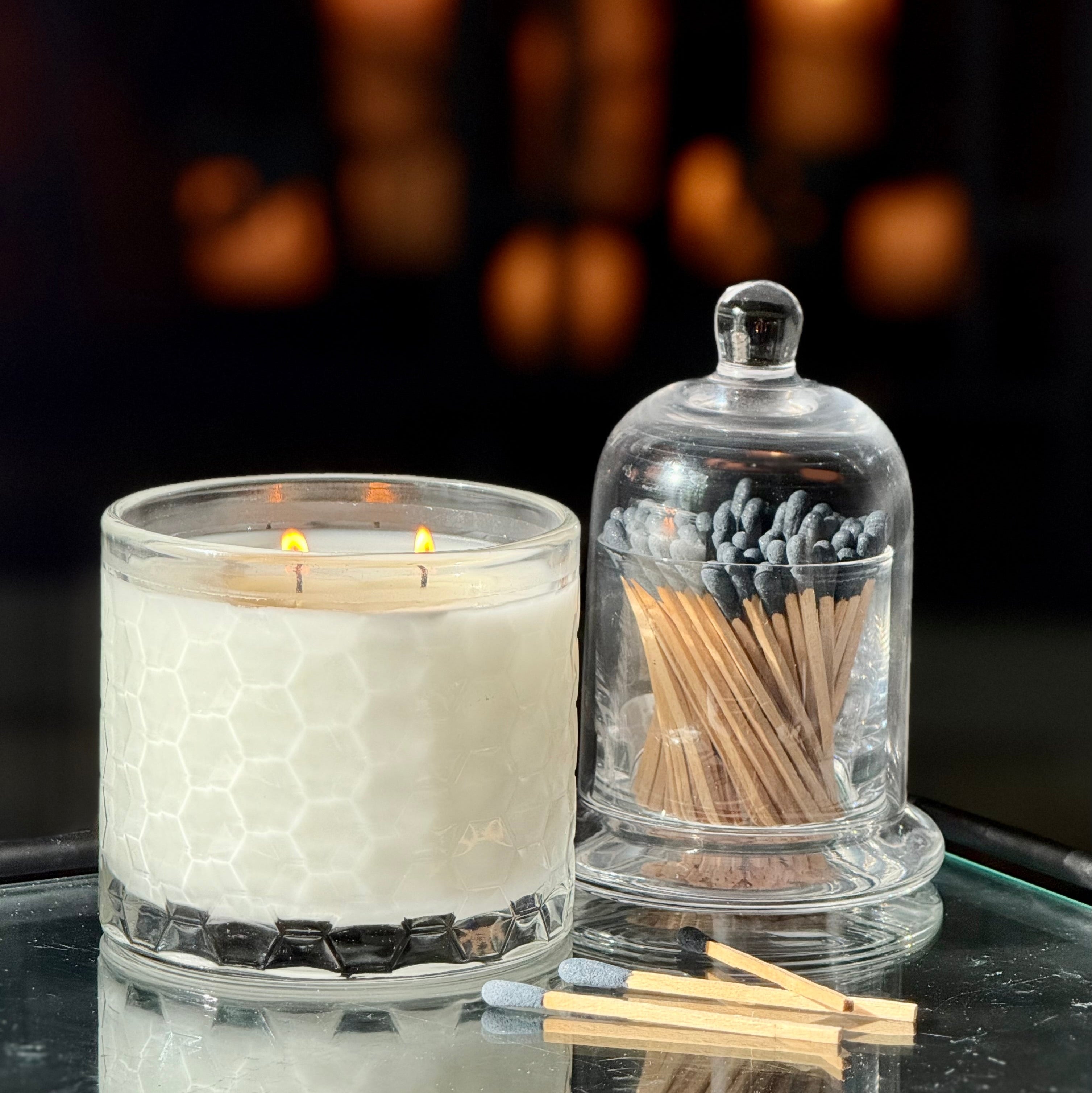 Candle and glass container with matches on a reflective surface with a blurred background
