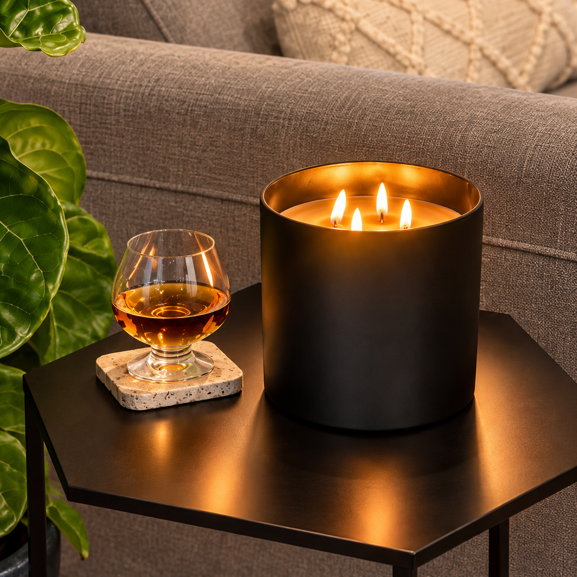 ELDé Fireplace Candle with four glowing wicks in a matte-black vessel, displayed beside a glass of amber spirits on a black side table.