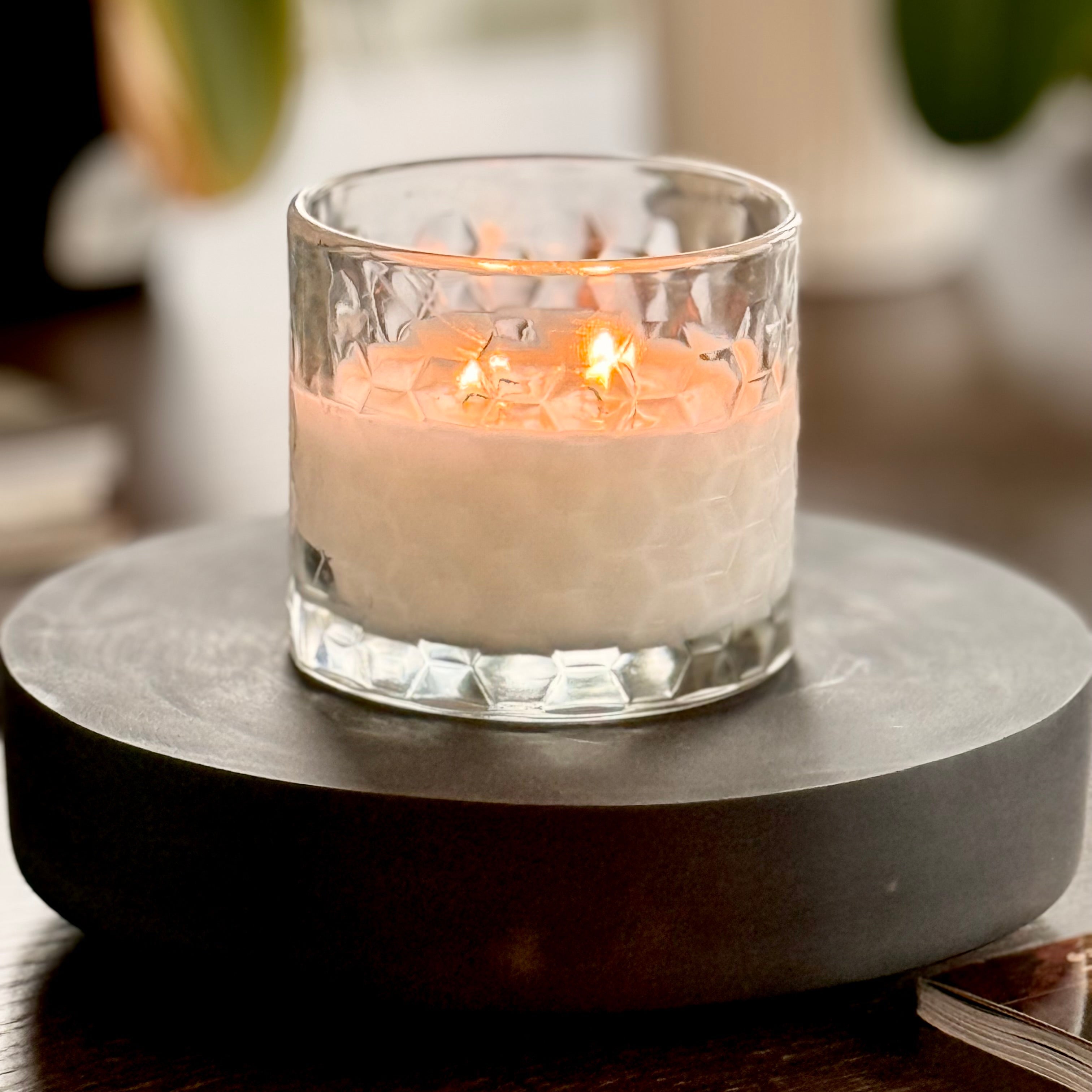 Candle in a glass holder on a dark stone coaster with a blurred background