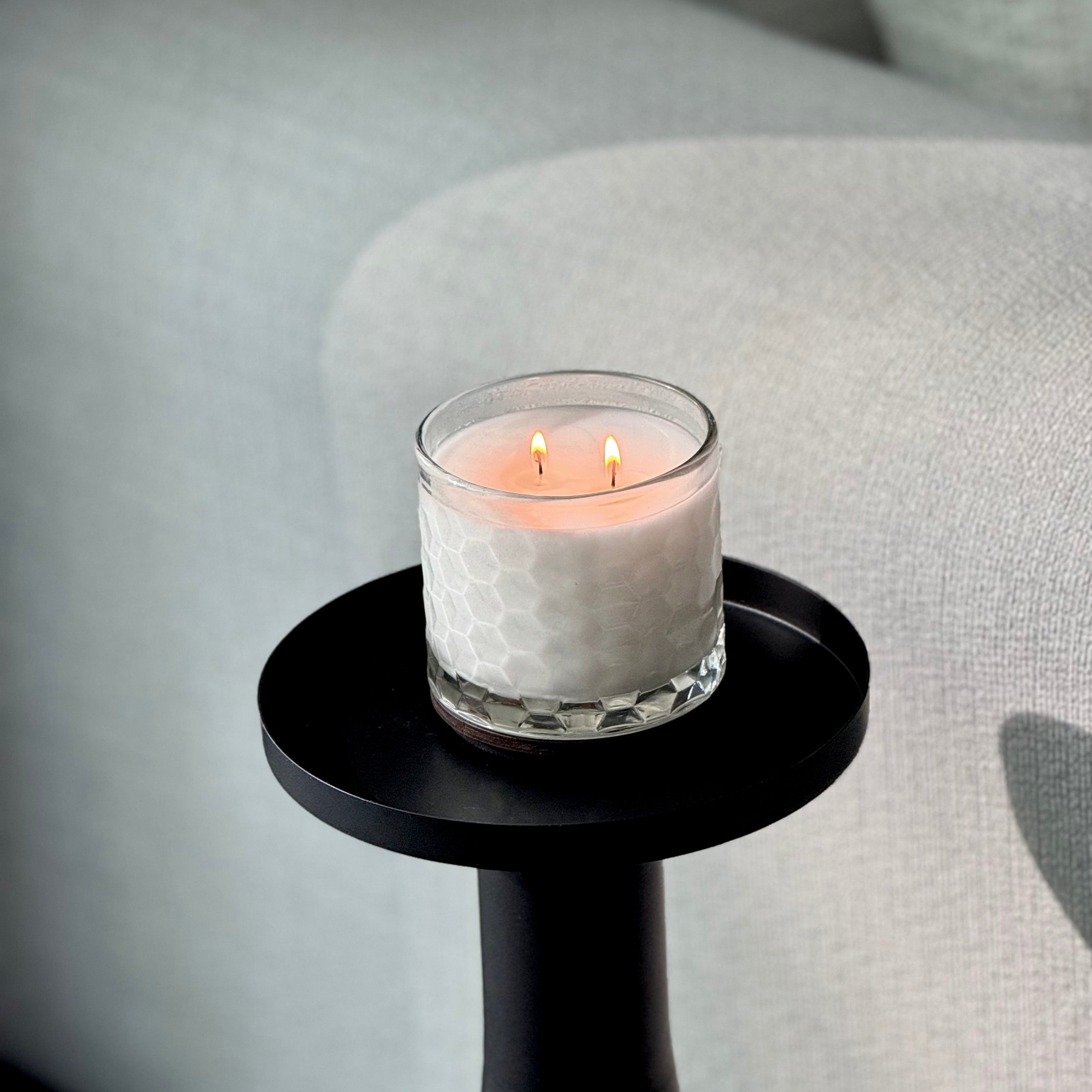 Candle in a glass holder on a small black table against a gray sofa background