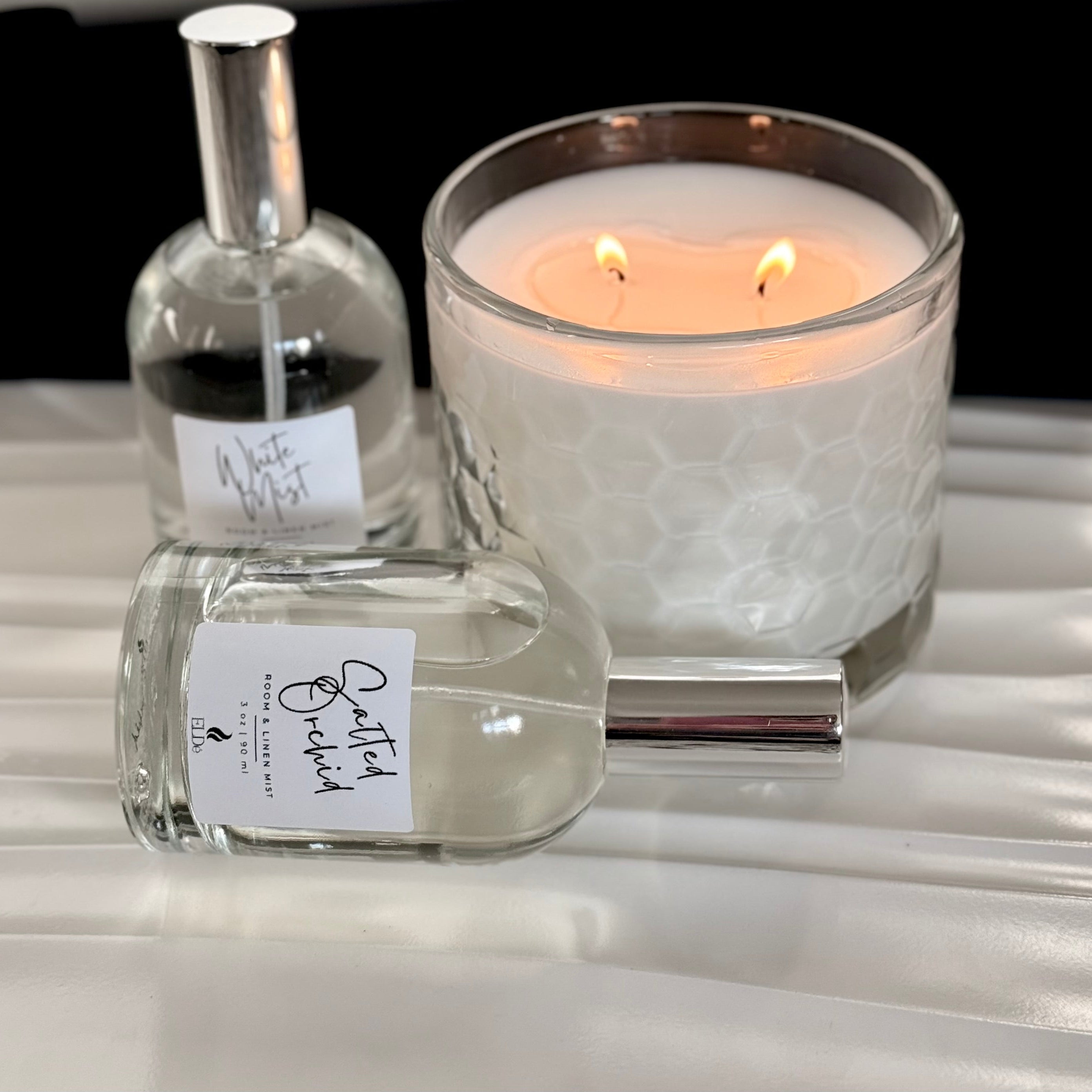 Two glass bottles with labels next to a lit candle on a reflective surface.