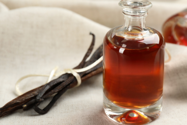 Glass bottle of vanilla extract with vanilla beans on a beige cloth background