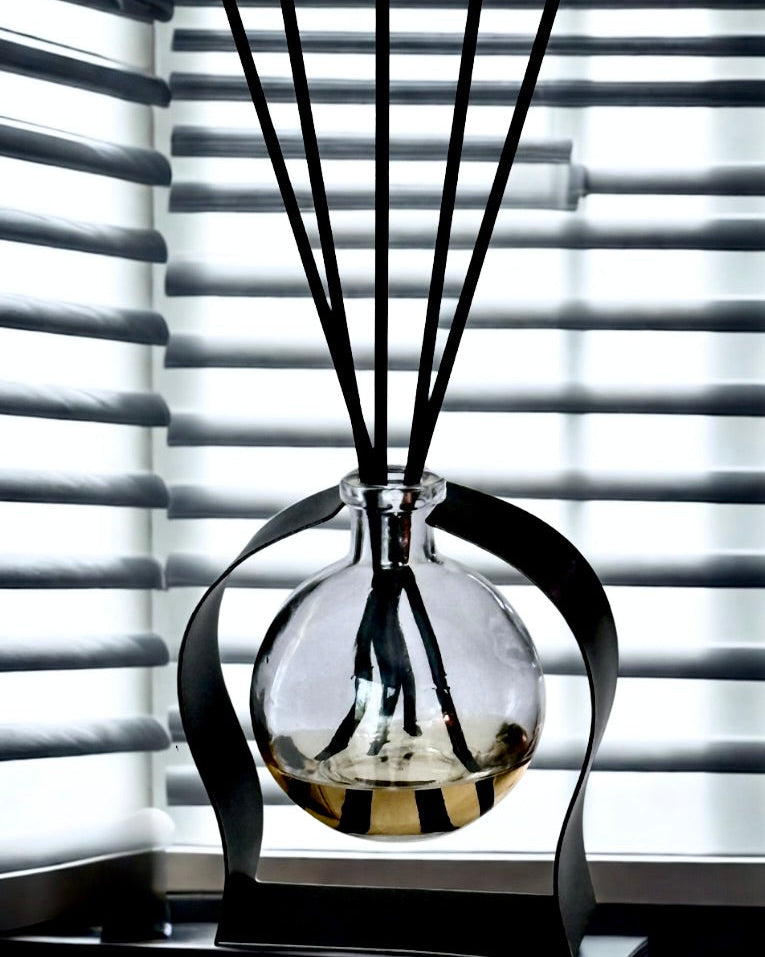 Glass diffuser with black sticks against a window with blinds