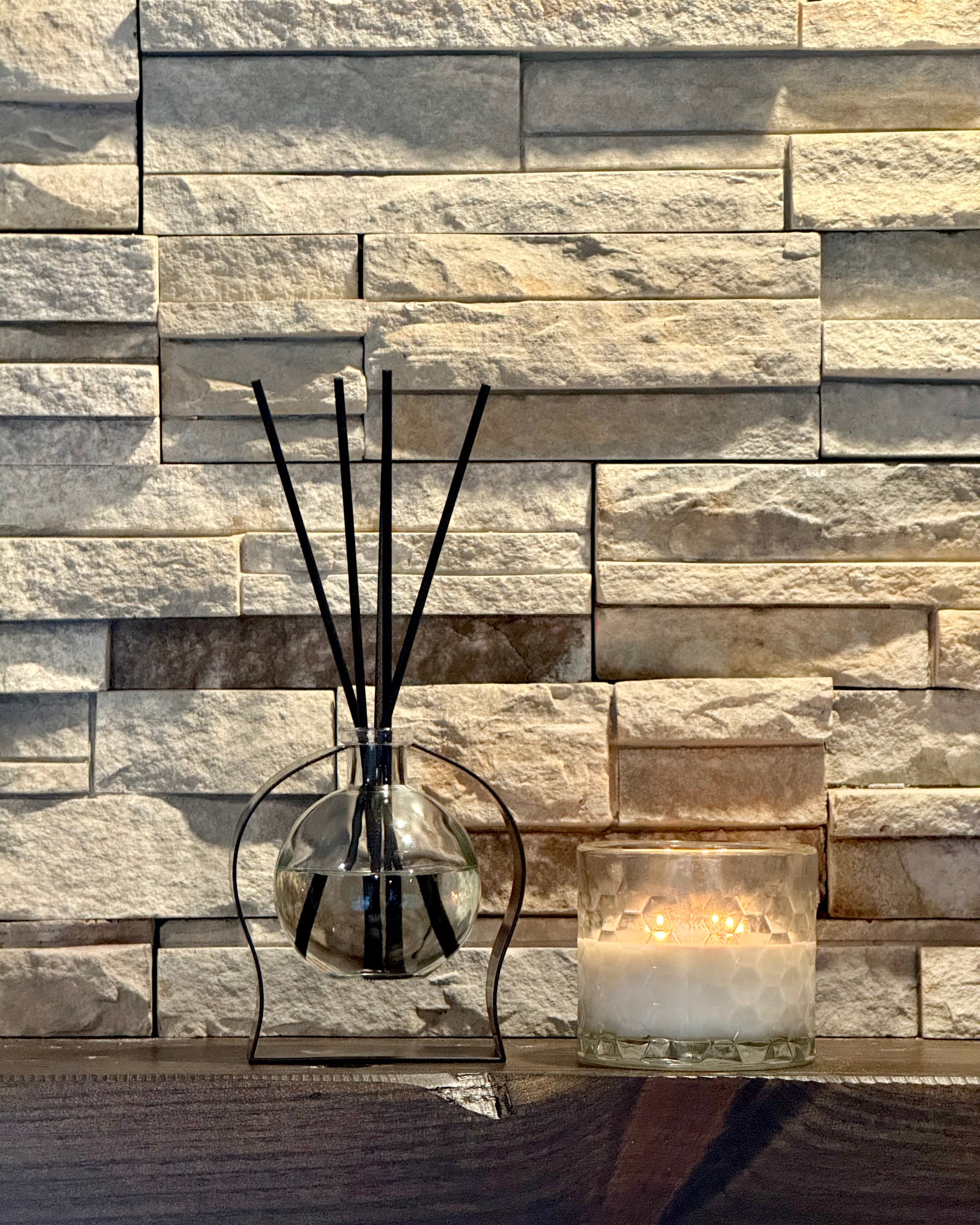 Decorative diffuser with reeds and candle on a stone wall background