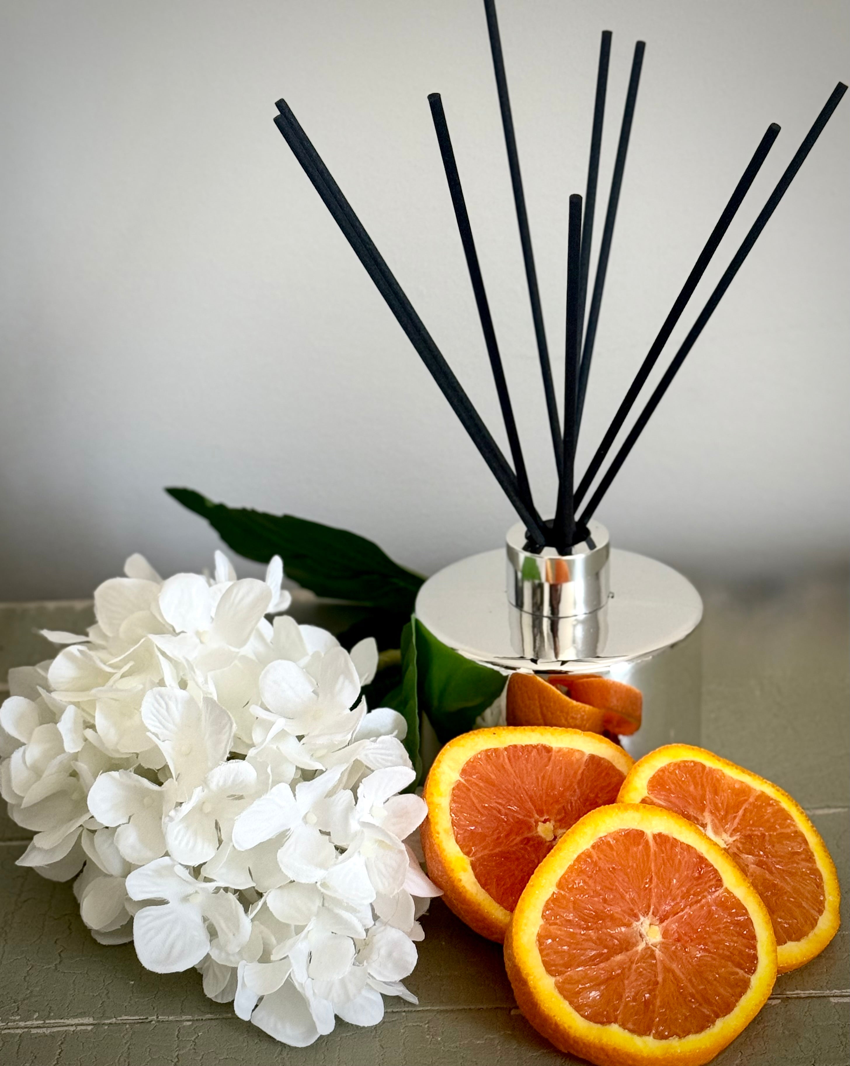 Diffuser with black sticks, white flowers, and sliced oranges on a gray surface.