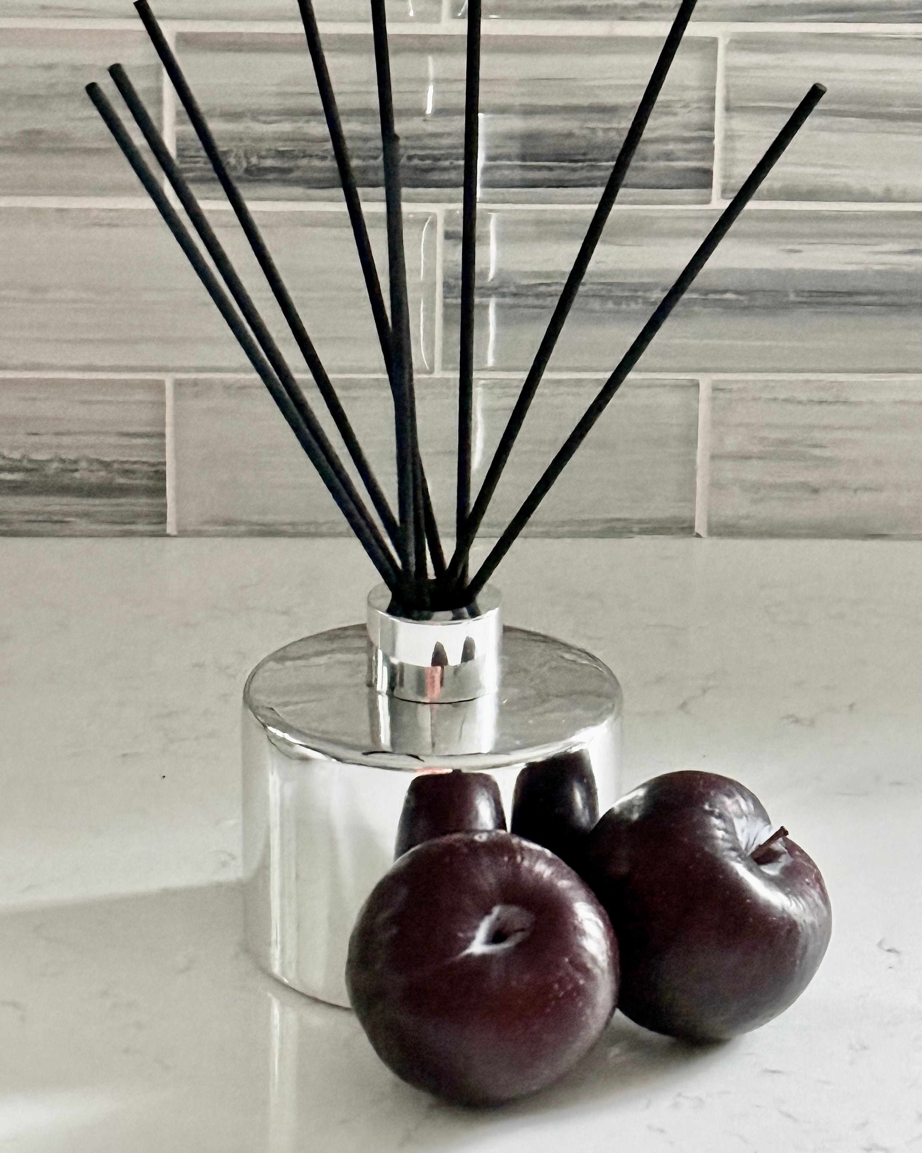 Silver diffuser with black sticks on a white surface with plums