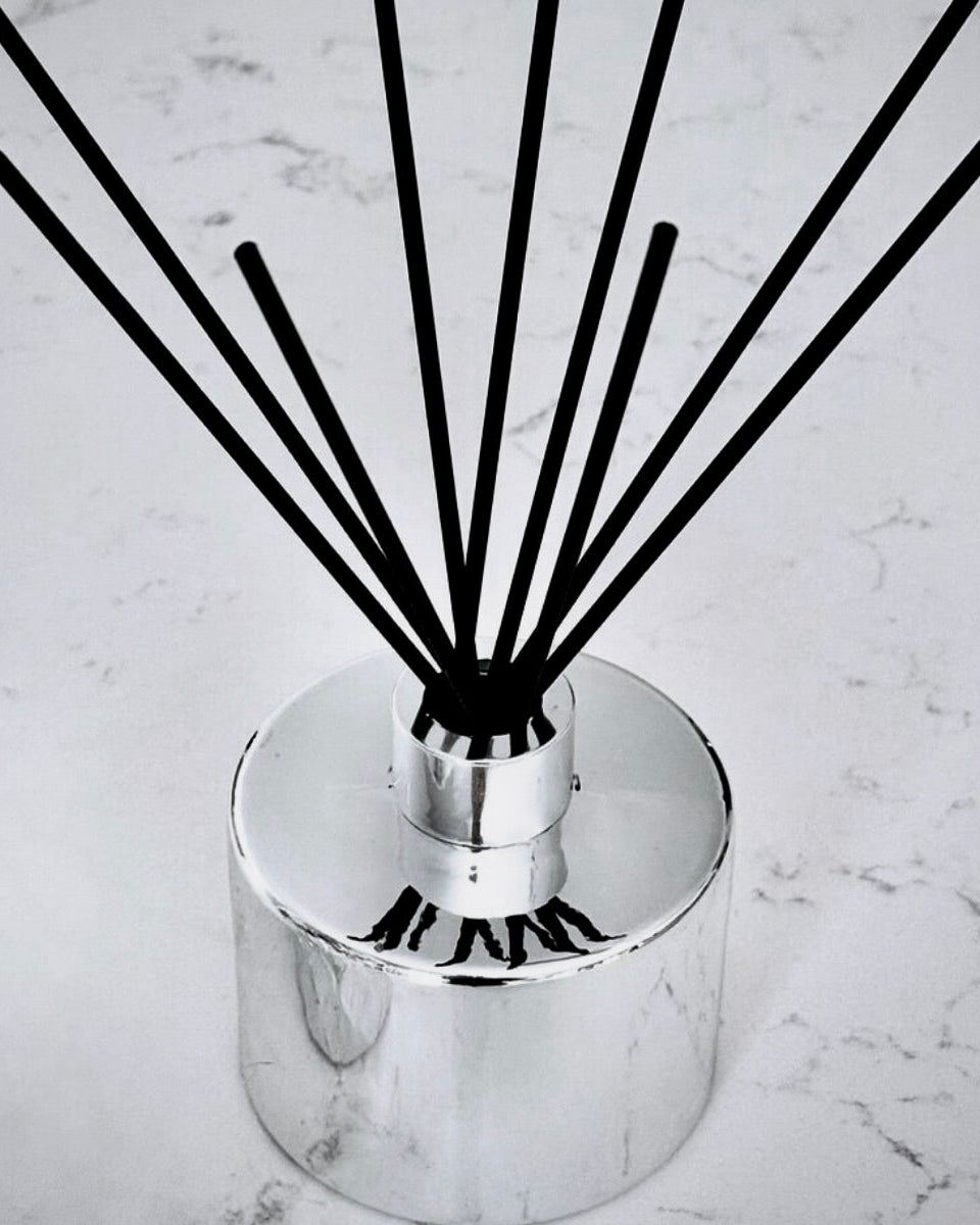 Reed diffuser with black reeds in a silver container on a marble surface
