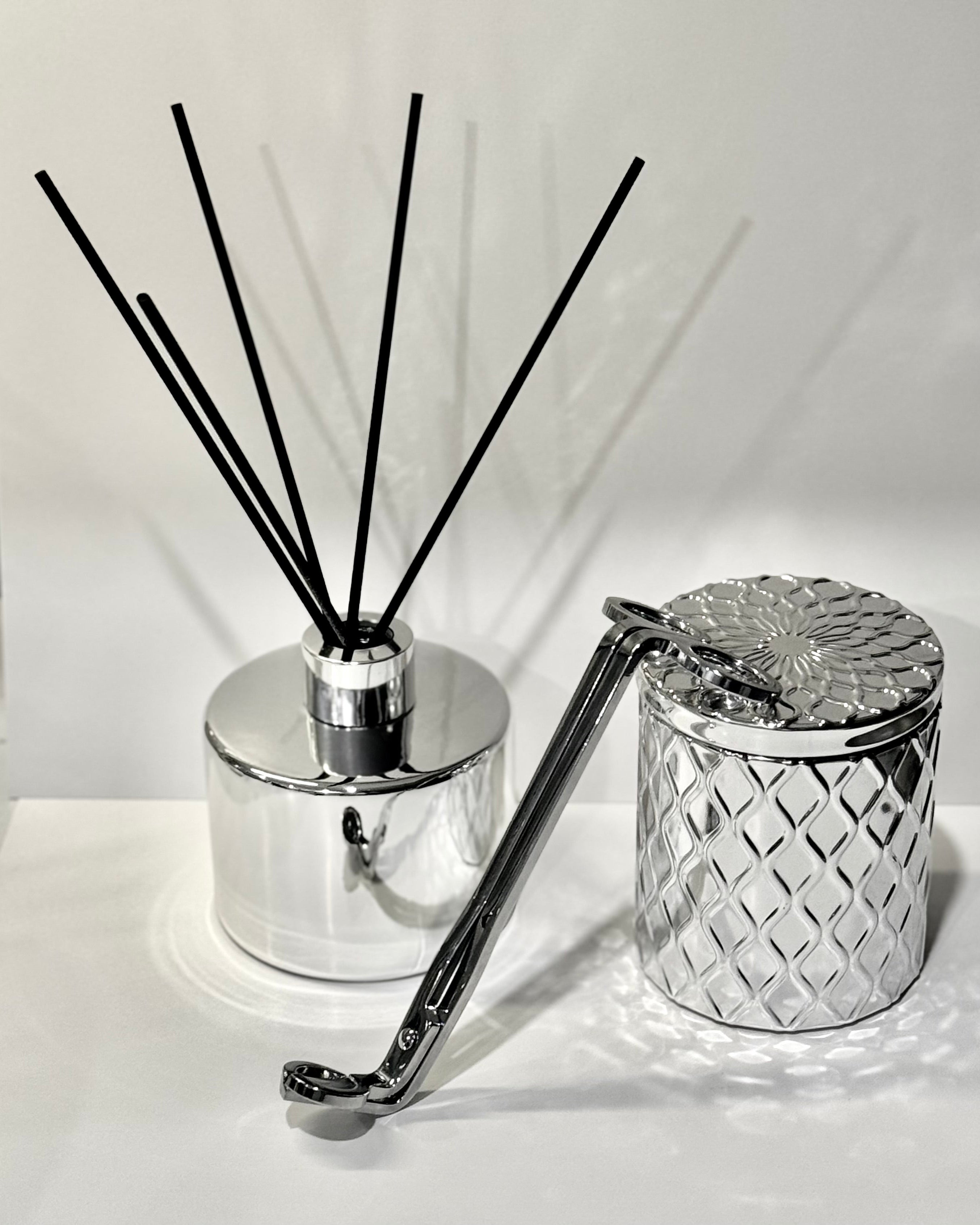 Silver diffuser with black reeds and a decorative container on a white background