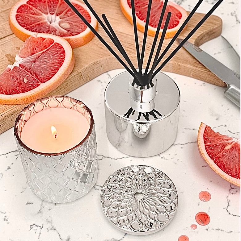 Diffuser with black reeds, lit candle, and grapefruit slices on a marble surface